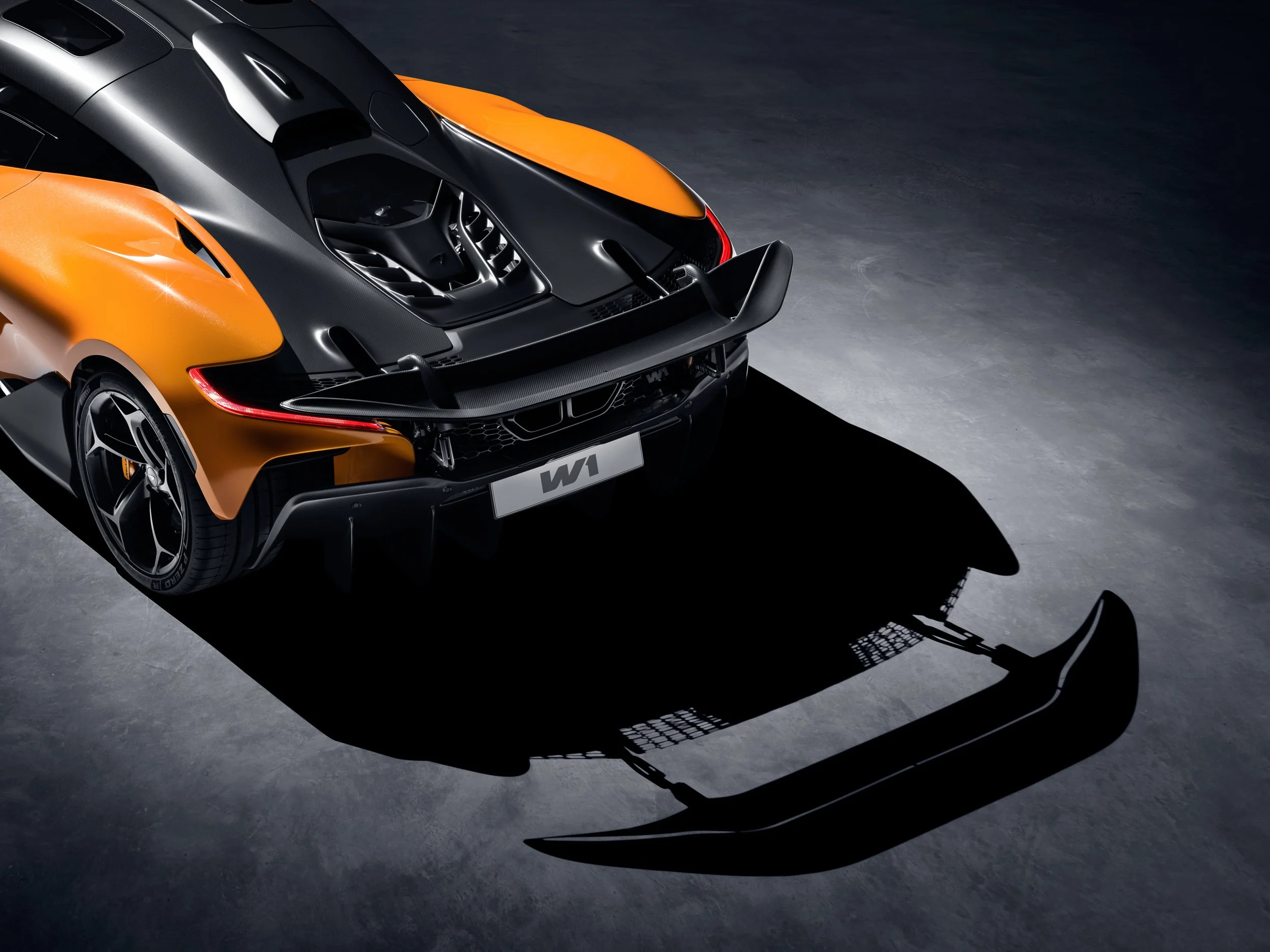 Rear view of an orange and black sports car with a large rear wing parked on a gray surface.