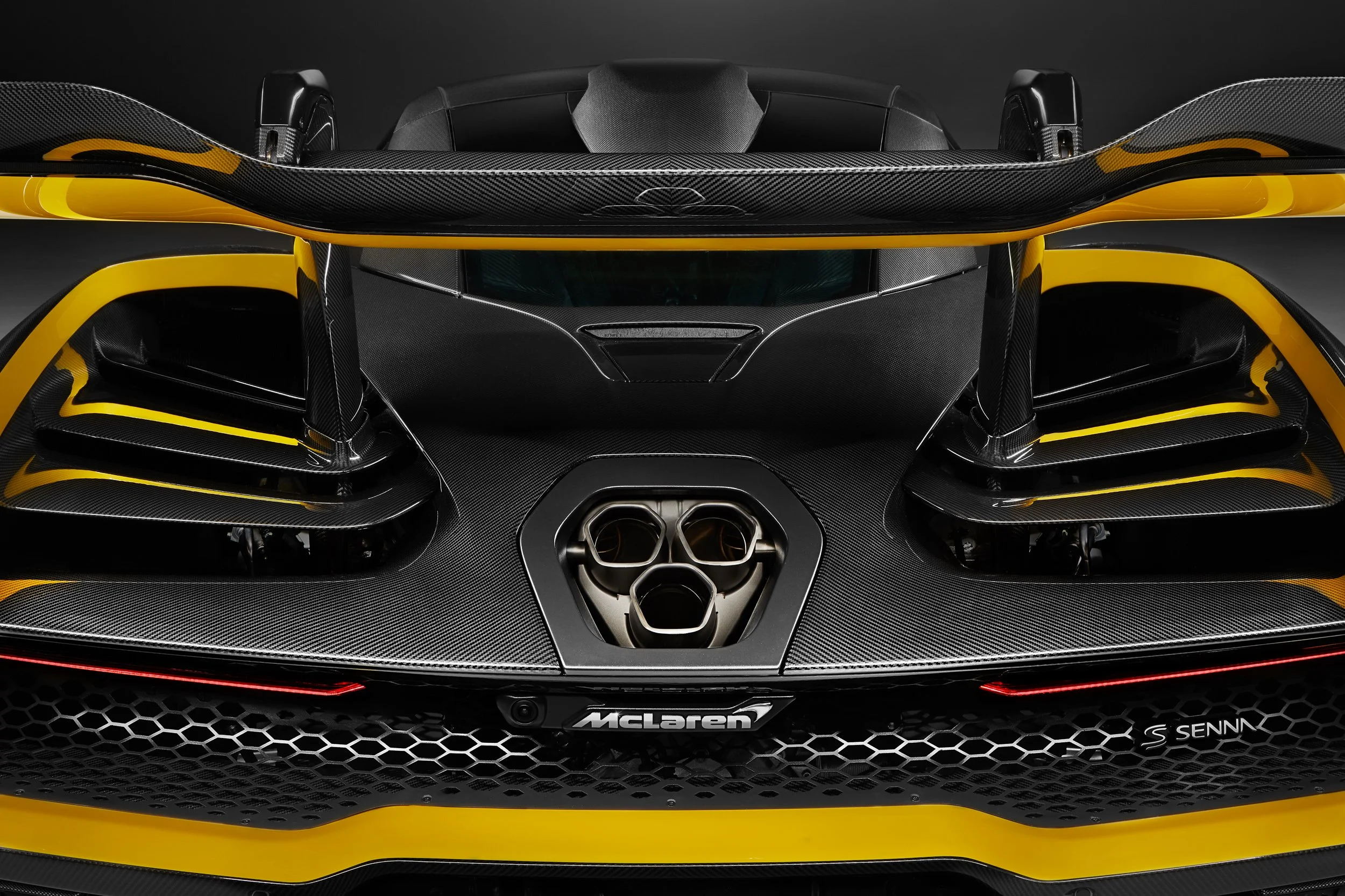 Rear view of a yellow and black McLaren supercar featuring a distinctive spoiler, two exhaust ports, and aerodynamic design elements.