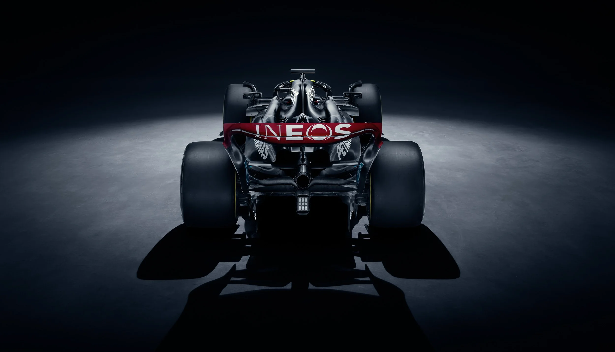 Rear view of a Formula 1 car with branding in a dimly lit setting.
