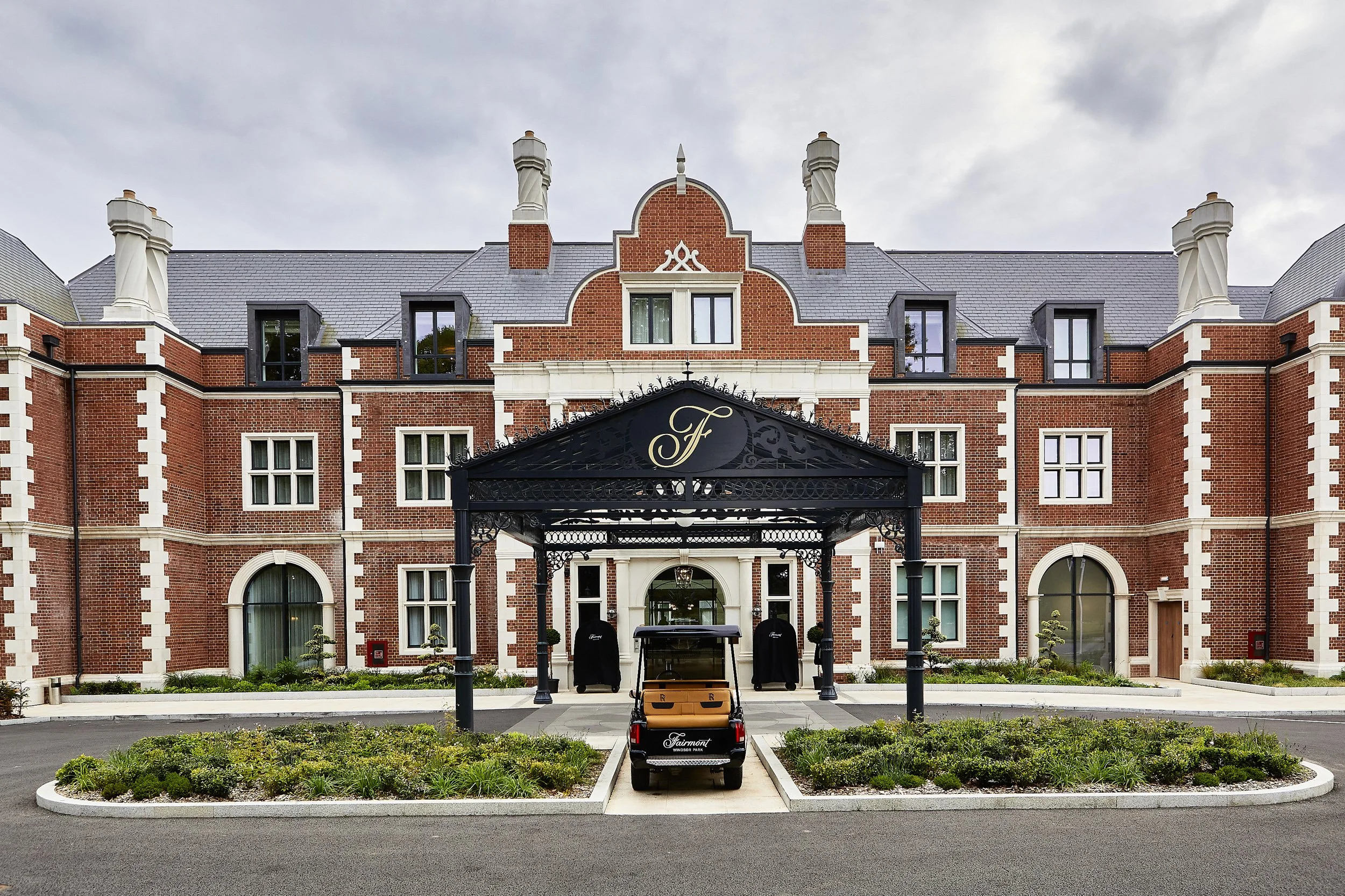 Exterior of a luxury hotel with a brick facade and a black metal canopy at the entrance, featuring a golf cart with a logo parked in front.