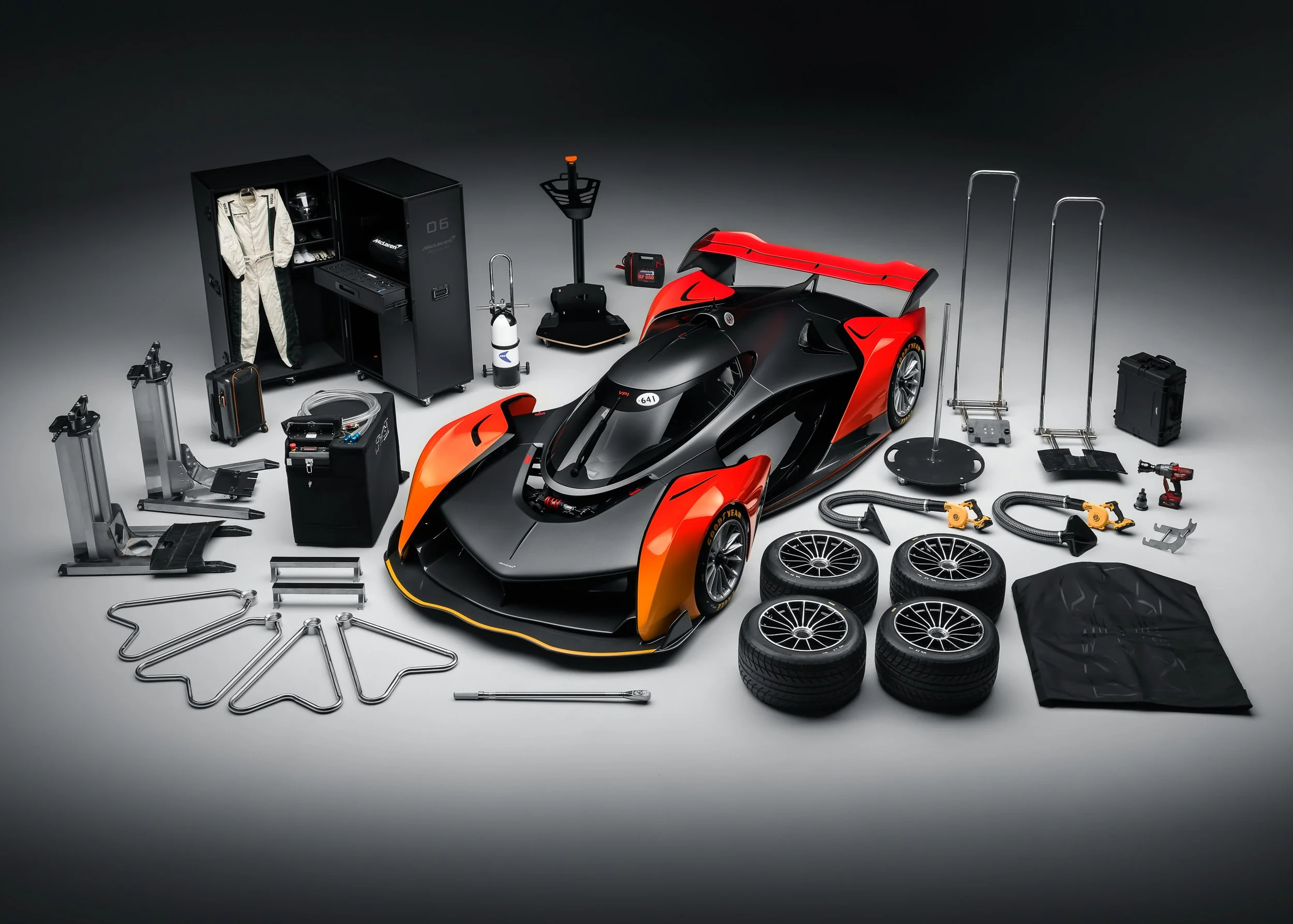 Race car surrounded by racing equipment, including four wheels, a suit, tools, and a storage cabinet.
