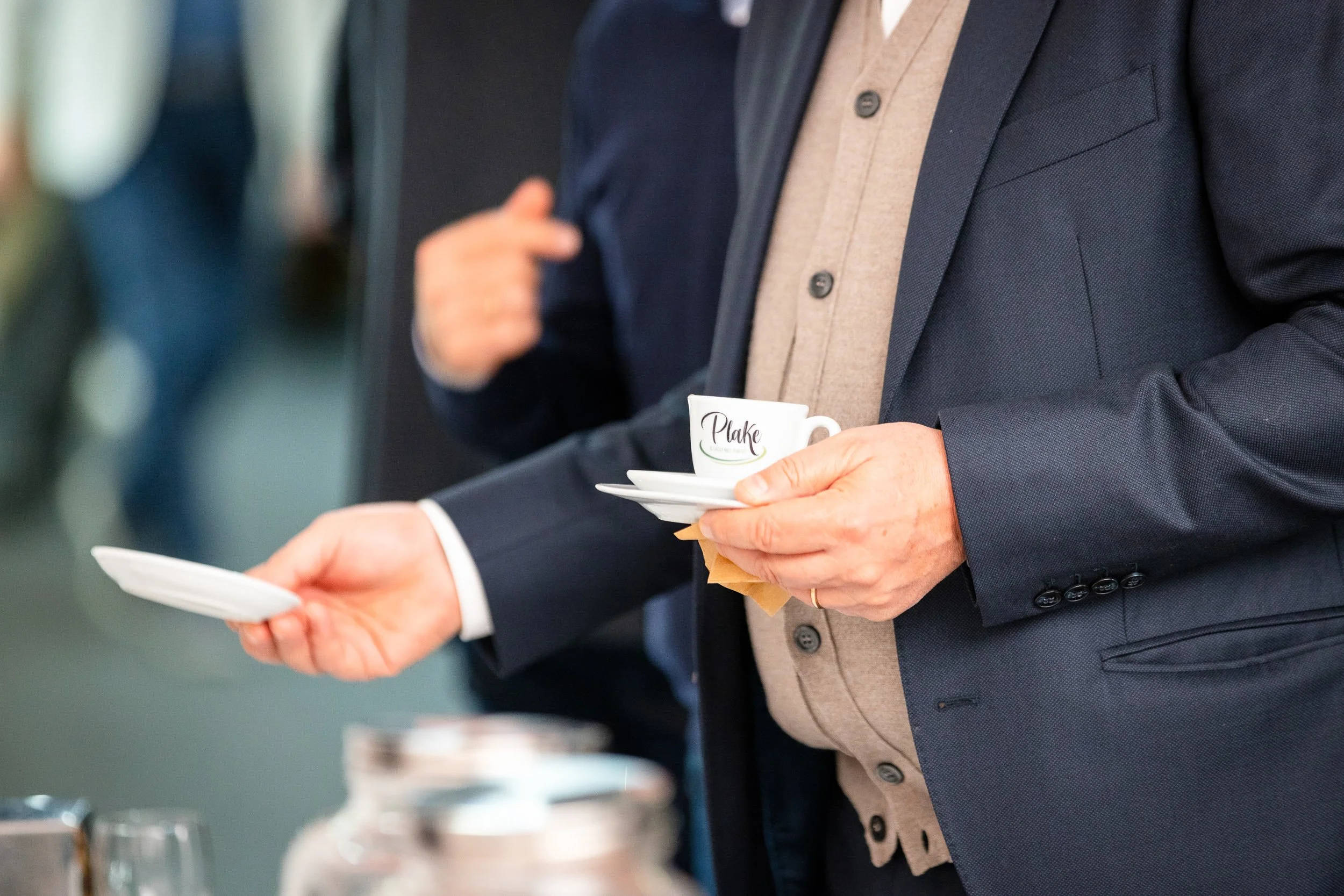 Person in a suit holding a coffee cup and saucer at an event.