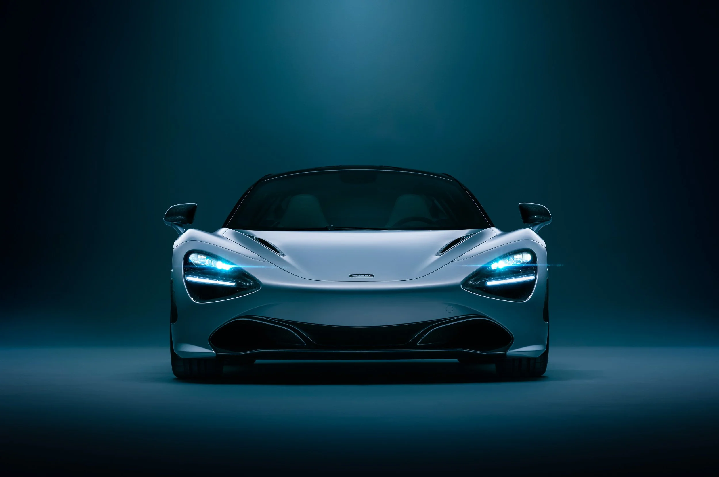Front view of a silver sports car with illuminated headlights in a dark studio setting.