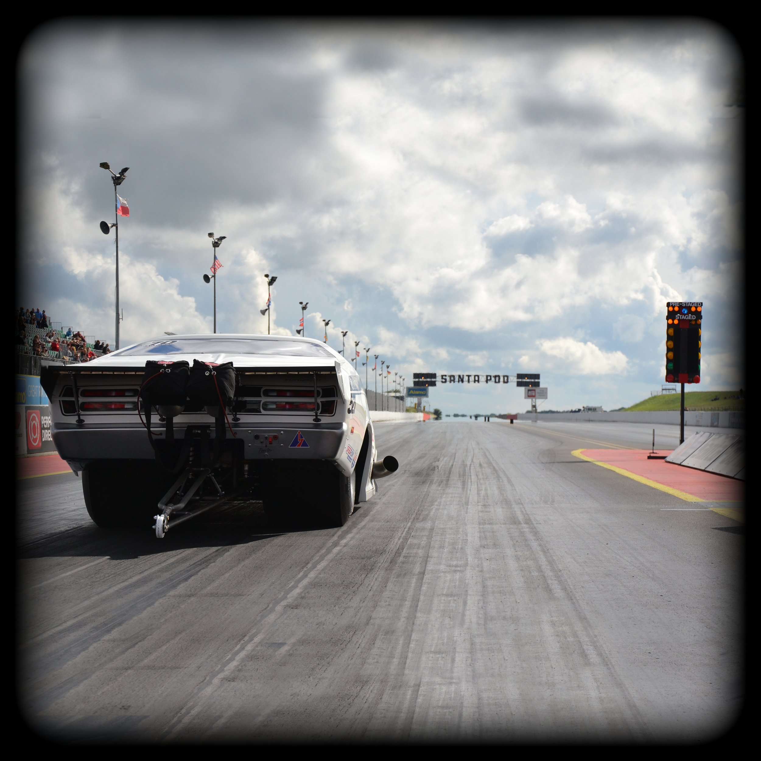 Plymouth Duster Pro mod Race car on the starting line at a dirt track racing event with a scoreboard in the background.