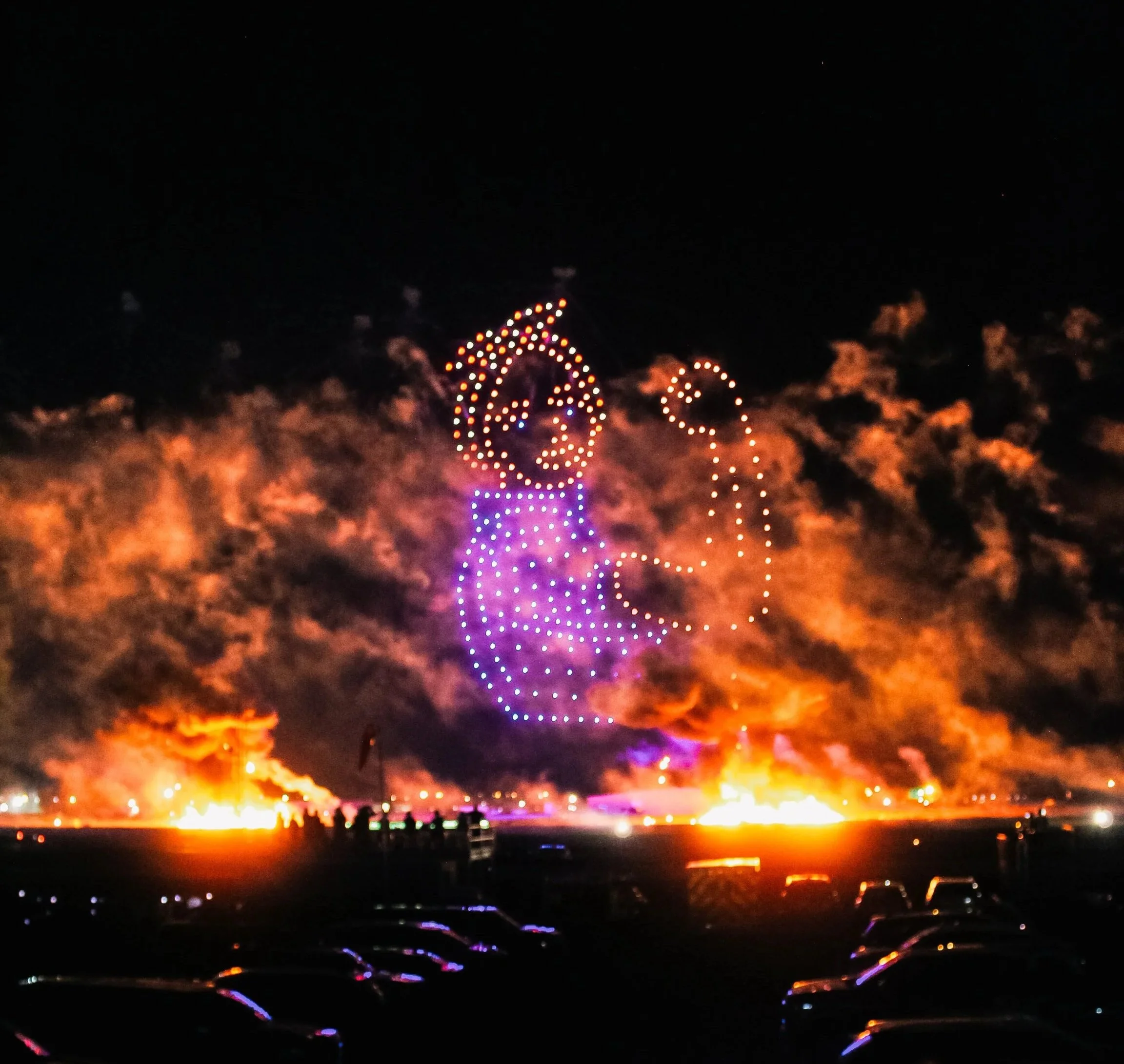 Drone aerial display in the night sky making a picture of rosie the riveter and framed with fireworks and pyrotechnics