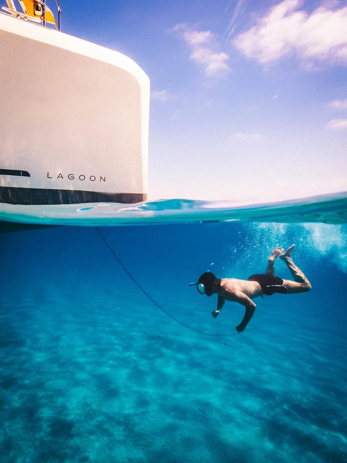 Professional underwater split-shot of a Lagoon catamaran in the Ionian Sea, featuring a diver and crystal clear blue water, captured by marine cinematographer Joe Snowdon.