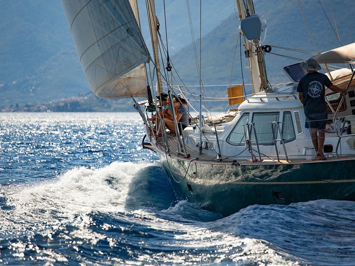 Professional regatta cinematography in Greece: A luxury classic sailing yacht heeling under full sail with a large bow wave, captured from a chase boat for maritime event coverage.
