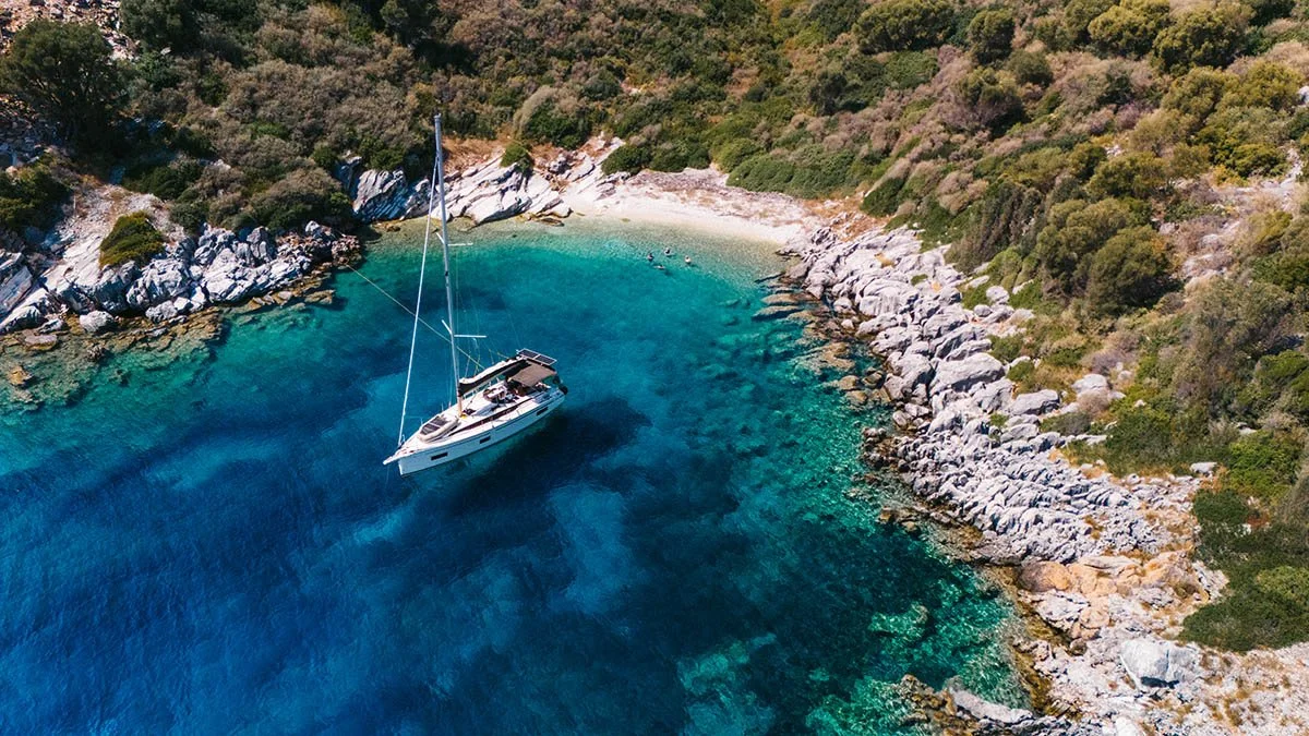 High-angle aerial photo of a luxury sailing yacht at anchor in a crystal-clear Lefkada cove. Professional Ionian yacht photography and drone videography services in Greece.