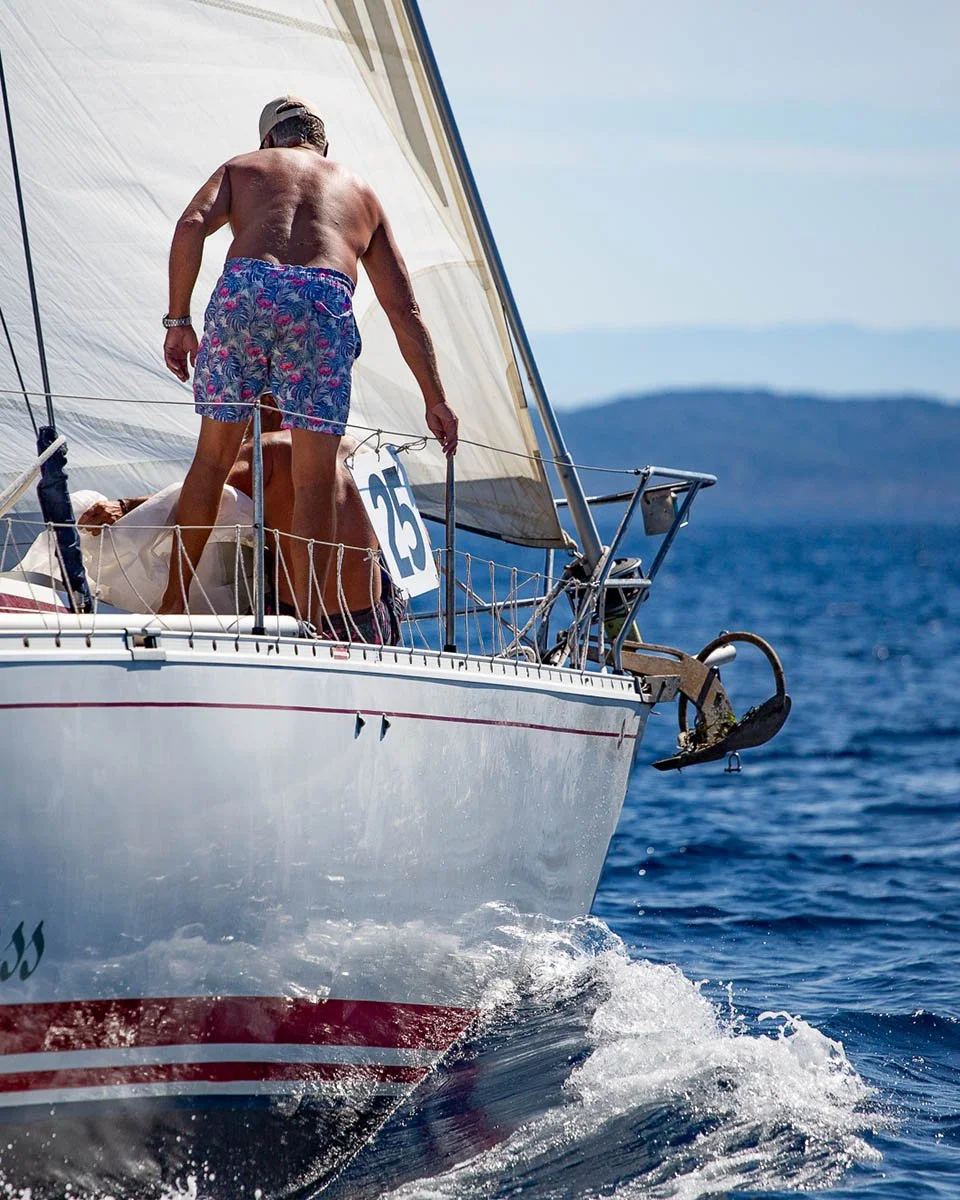 Action cinematography of a sailing yacht competing in the Southern Ionian Regatta near Lefkada, Greece, showing crew on the bow and the hull cutting through blue water.