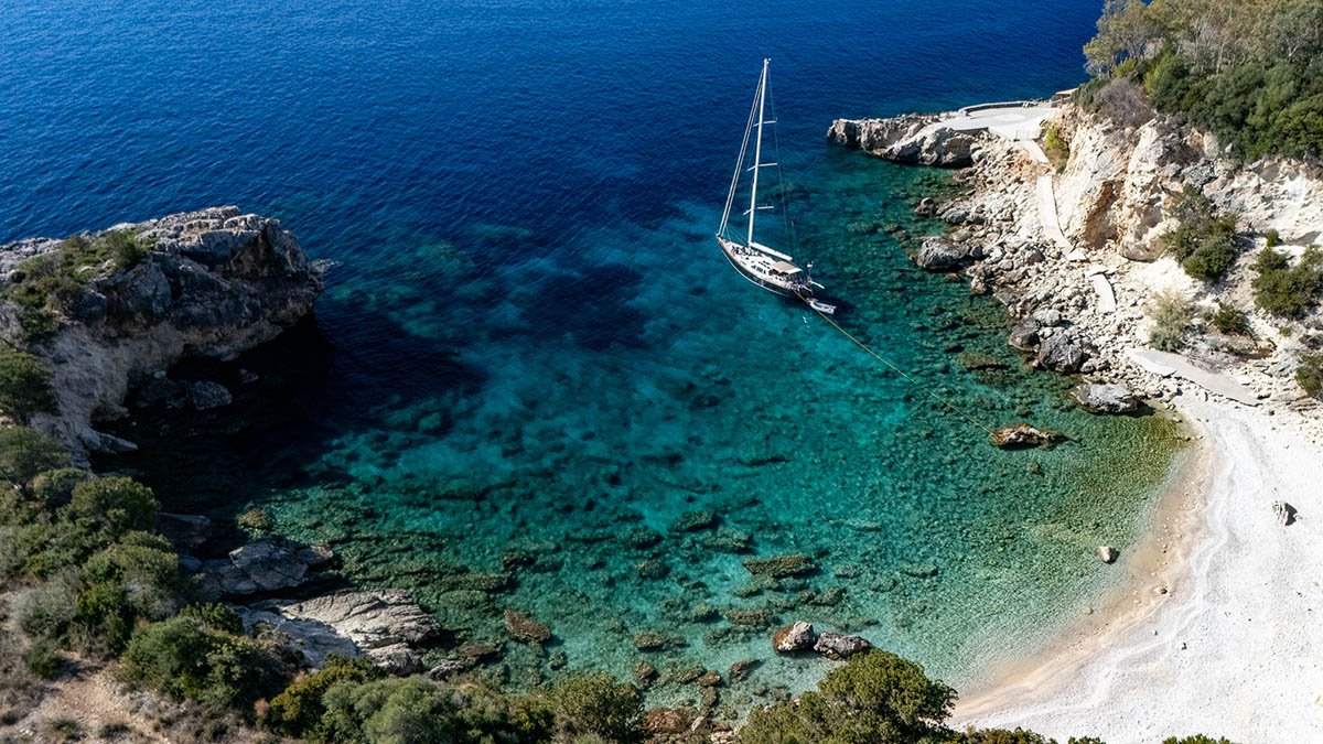 Aerial drone cinematography of a sailing yacht anchored in a secluded turquoise bay in Lefkada, Greece, for the maritime documentary 'Ionian Story'.