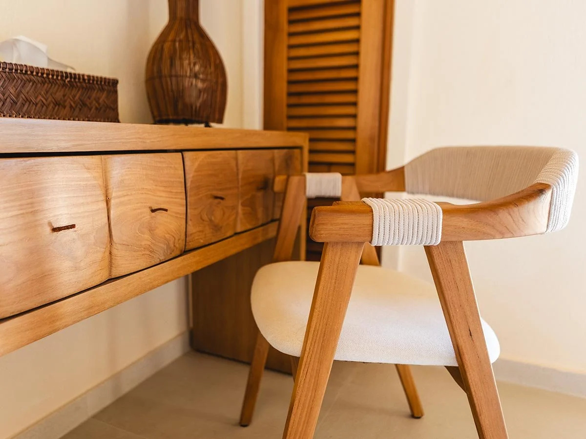 Detailed interior media from a luxury Ionian villa, showcasing the rich texture and craftsmanship of a sculpted wooden console, a modern cane and wood chair, and a woven decorative vase, illustrating natural Mediterranean design.