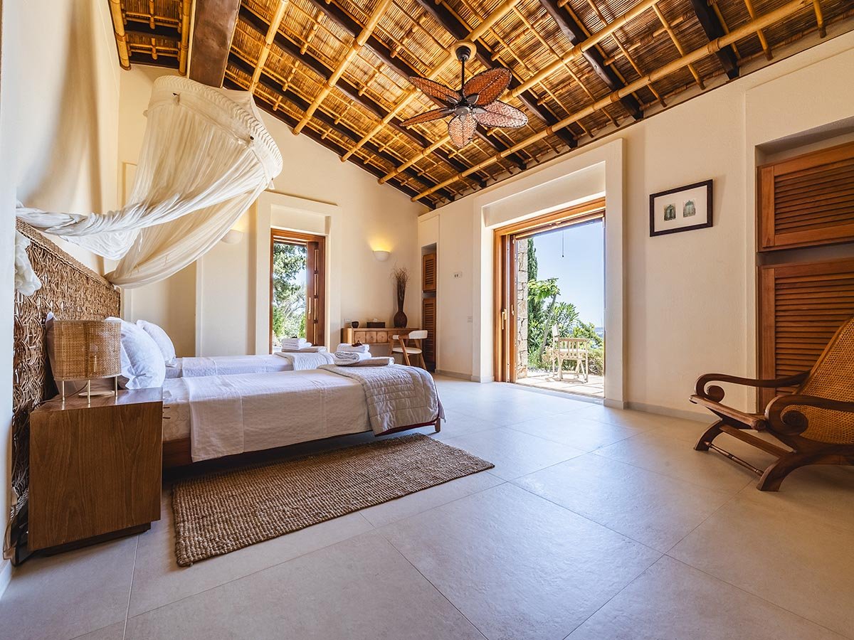 Professional real estate cinematography from an Ionian luxury villa, showcasing the seamless architectural flow from a light-filled bedroom with a traditional bamboo ceiling out to a private, sun-drenched sea-view terrace.