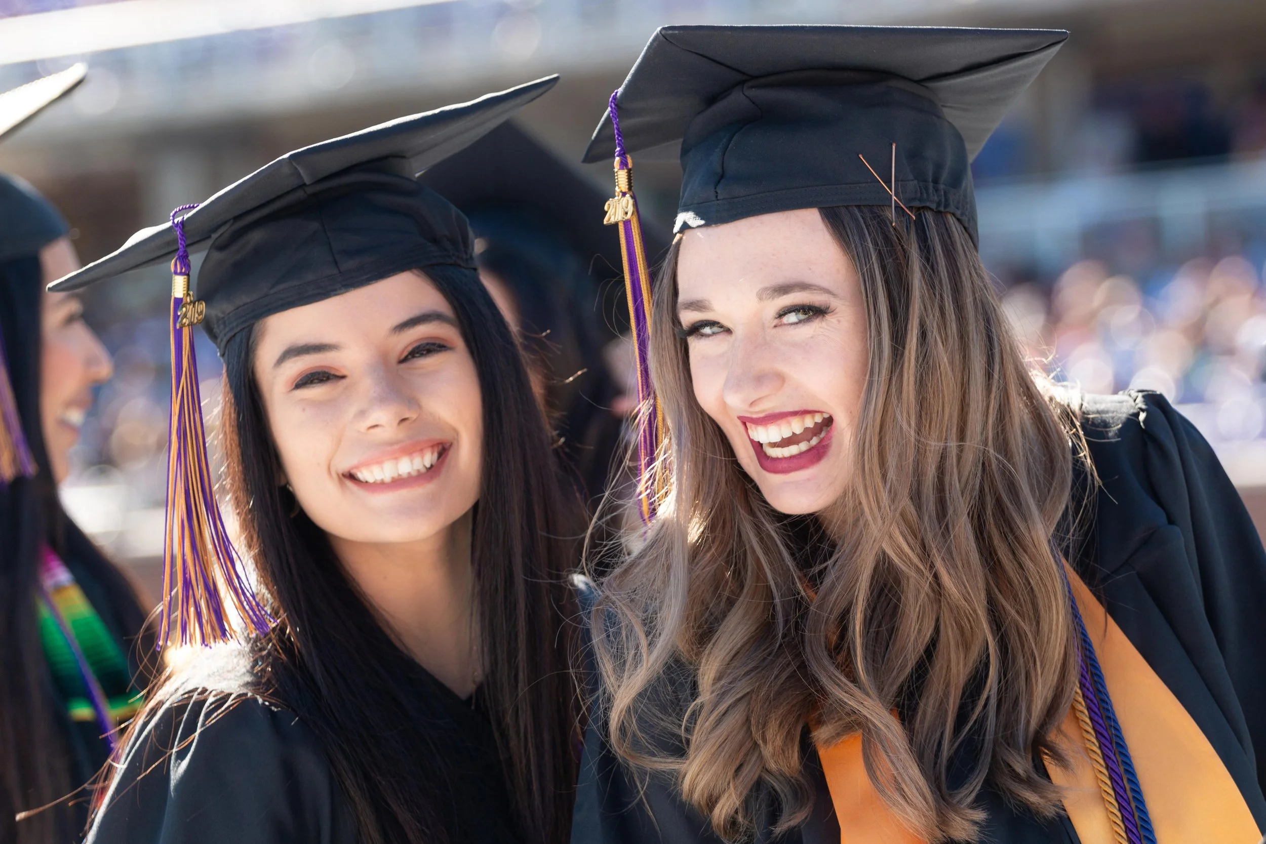 Two young women in graduation caps and gowns smiling and celebrating outdoors