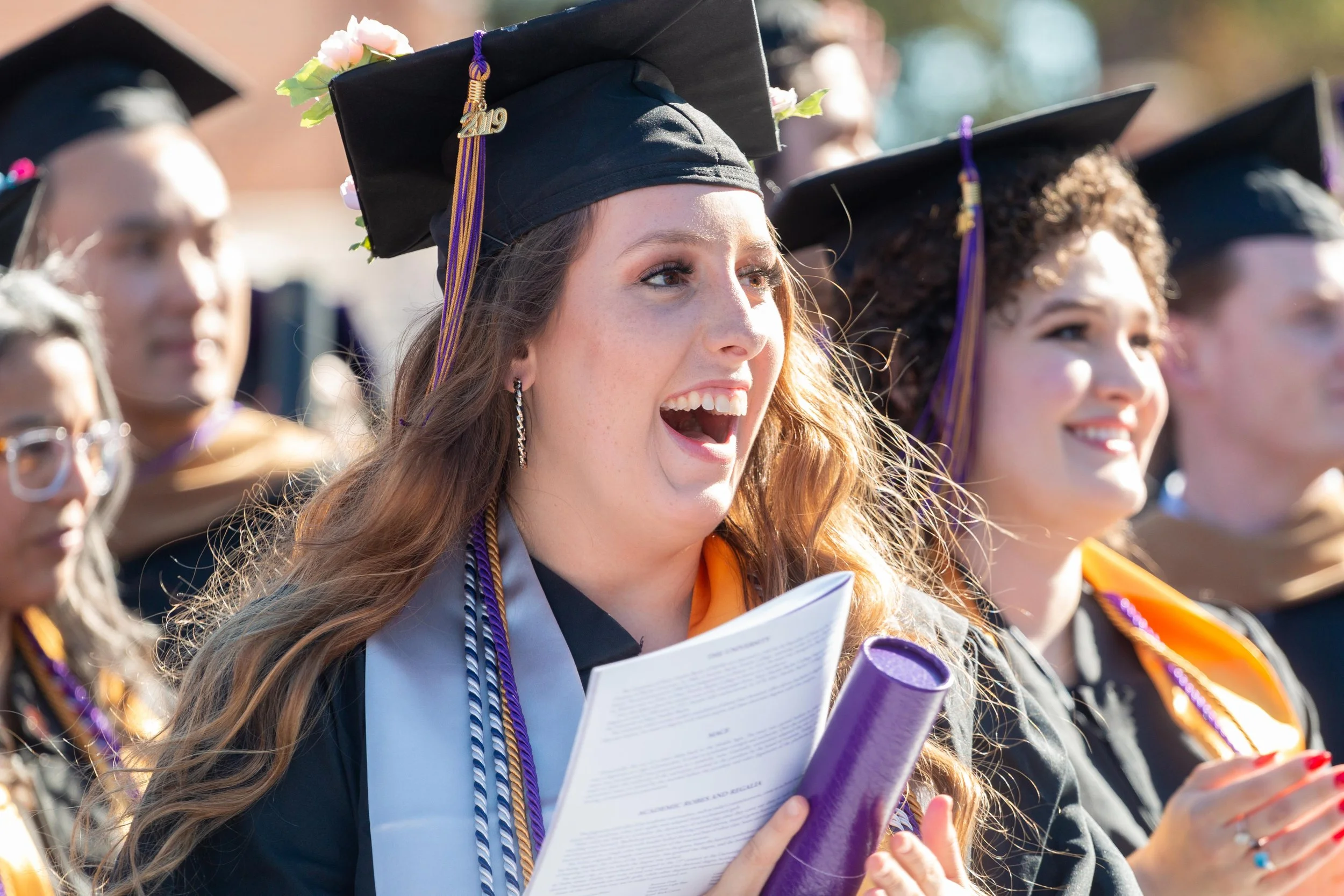 Group of diverse graduates in caps and gowns at graduation ceremony, smiling and celebrating outdoors.