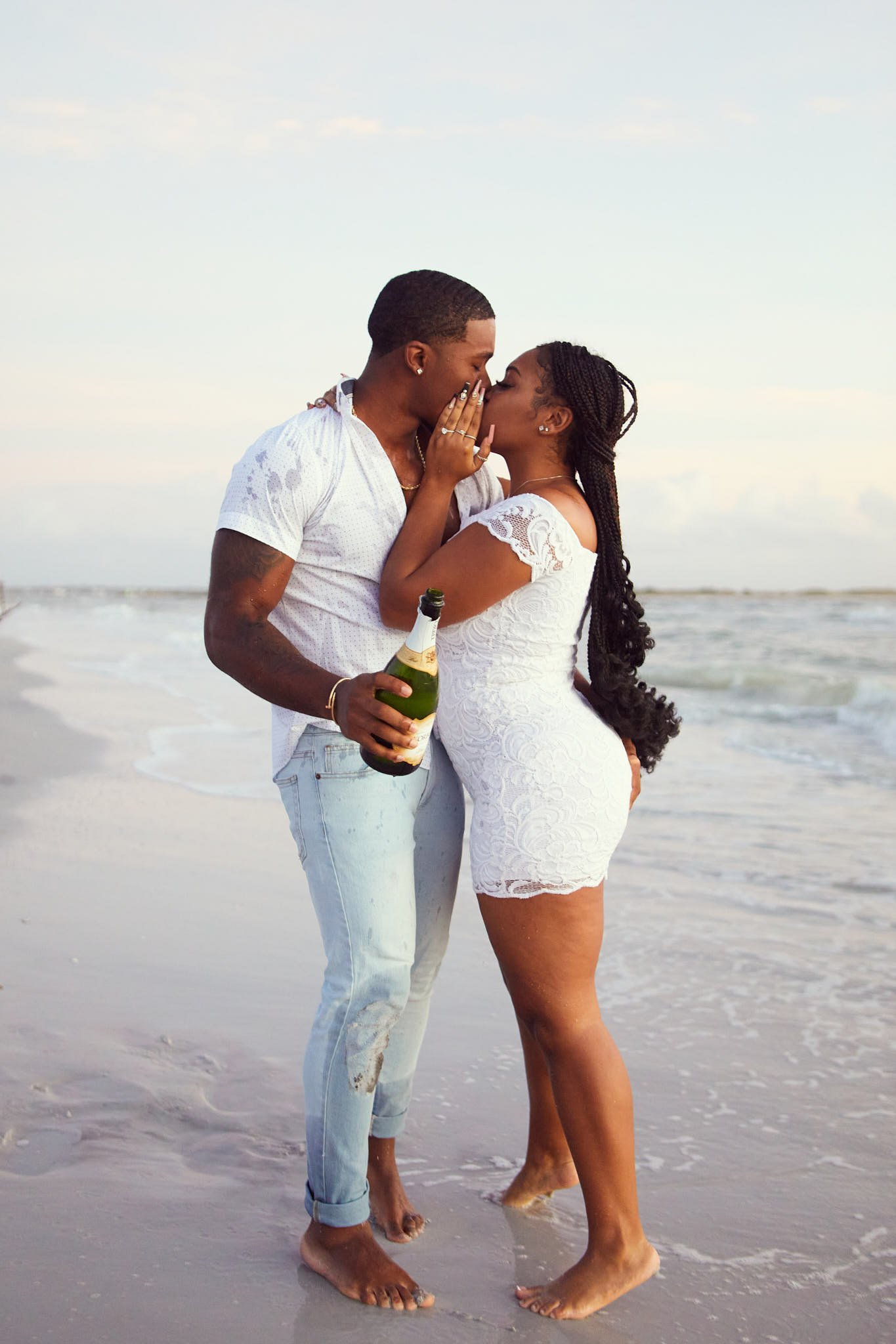 A couple kissing on the beach, with the man holding a bottle of champagne.