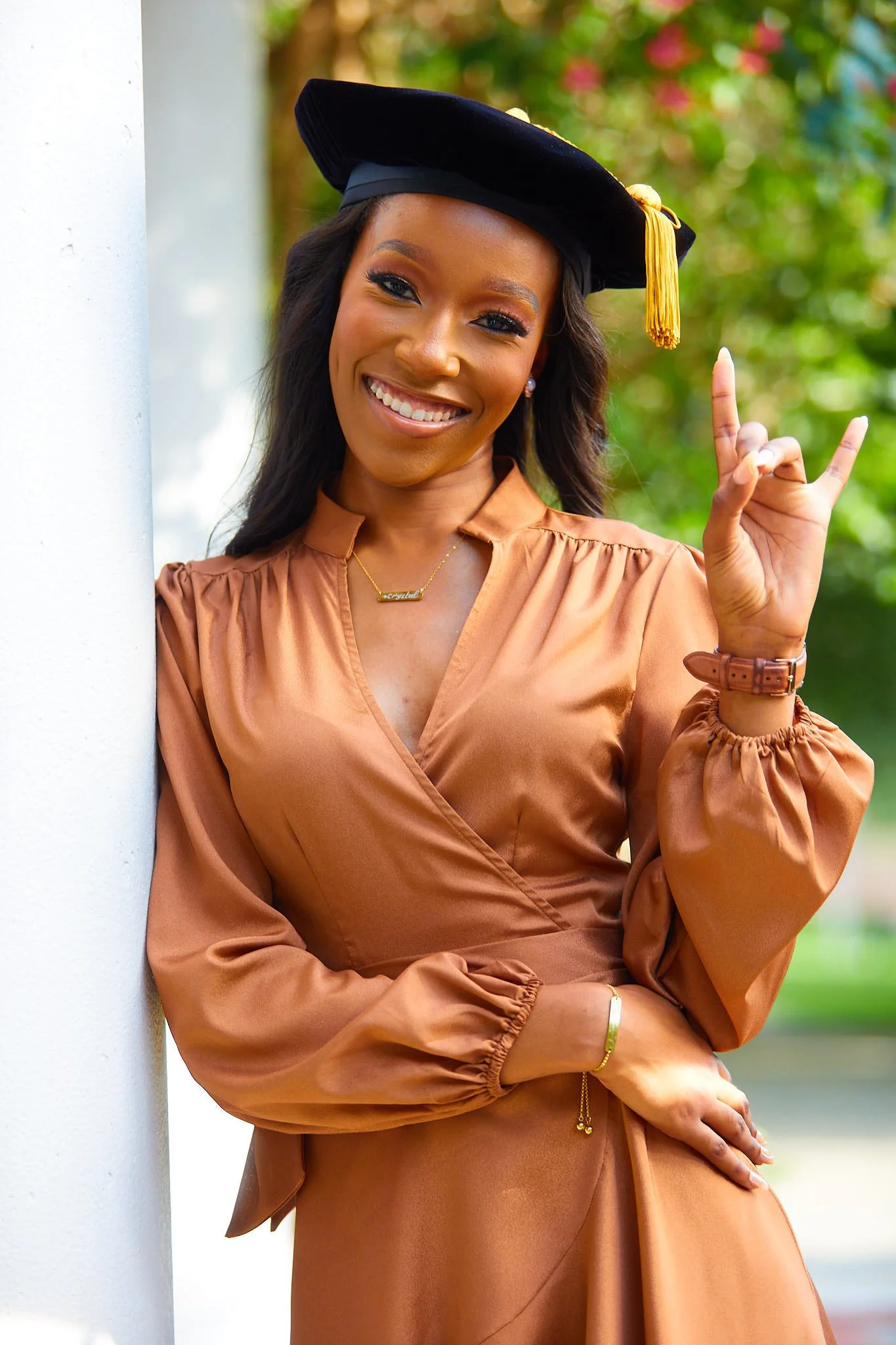 Graduation woman wearing cap and gown, smiling, making a rock on hand gesture.