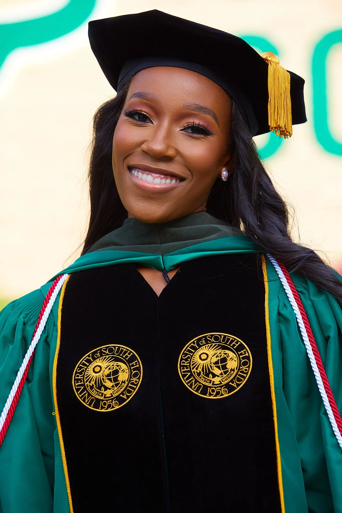 A smiling woman in a green graduation gown and cap at a university commencement ceremony.