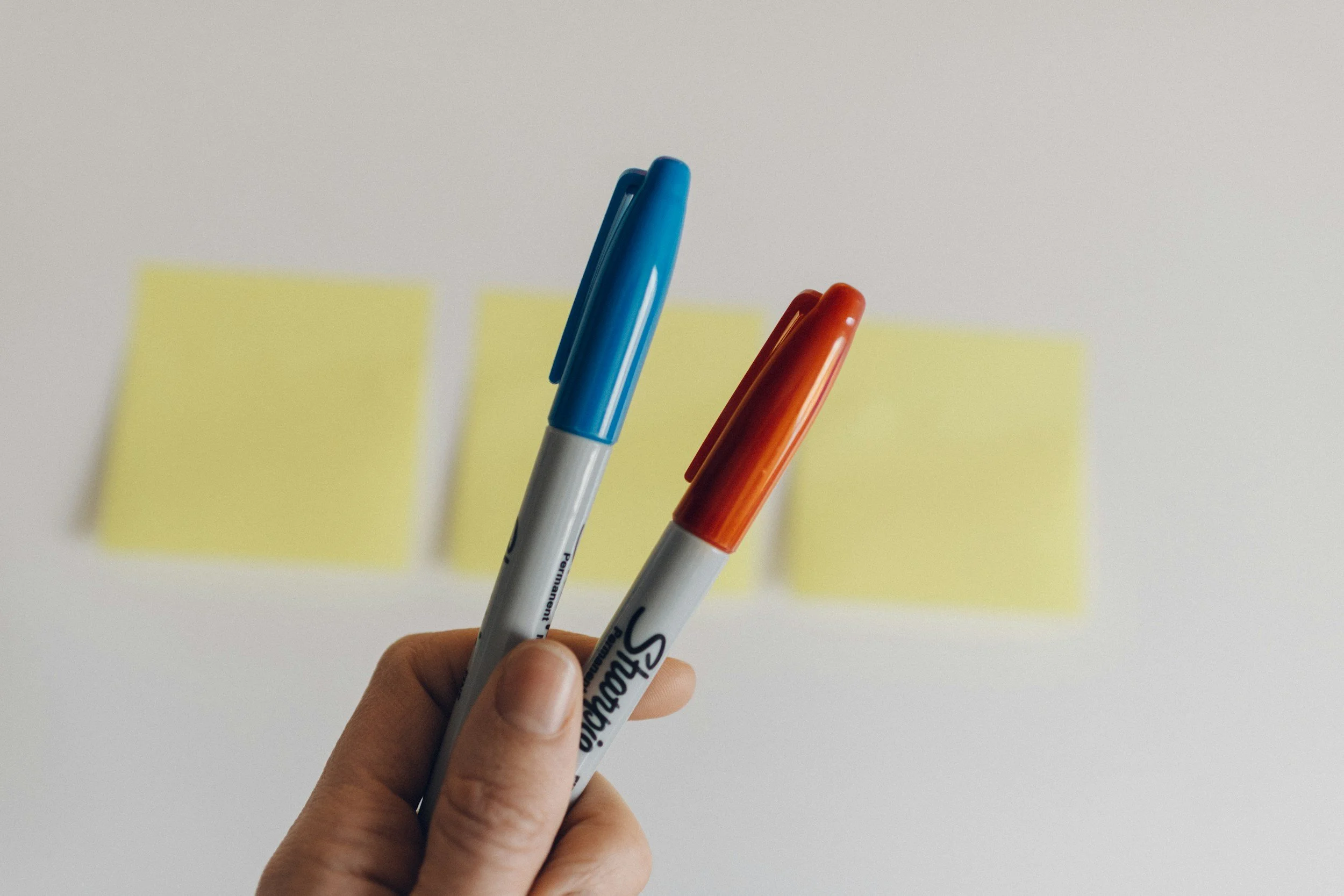 Two Sharpies are held in front of a wall with stickies. A workshop is held in the creative agency.