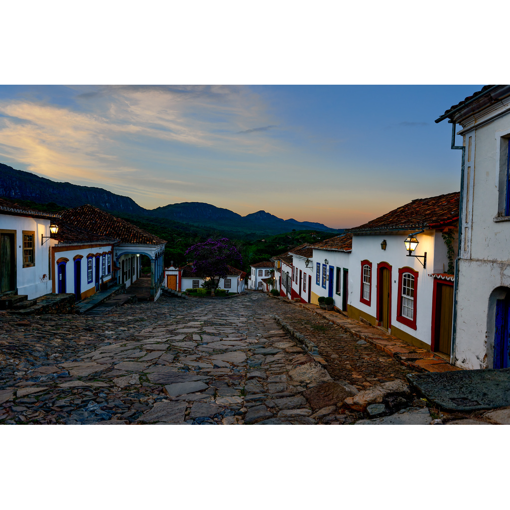 Golden Hour Glow – colonial cobblestone street in Tiradentes Brazil at sunset with warm light and mountains in background