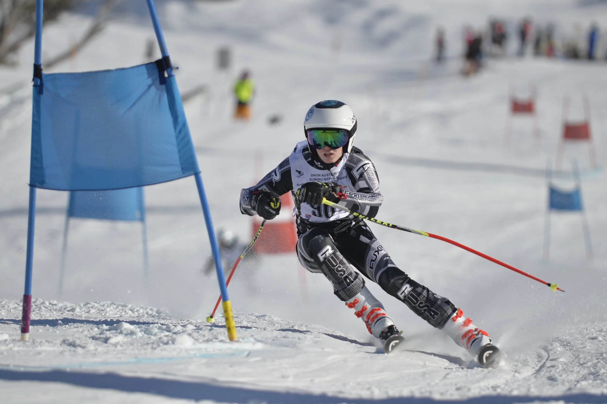 Snow Australia Interschools - ski racer on a course in perisher, wearing a helmet, goggles, and racing gear, navigating around blue slalom gate markers.