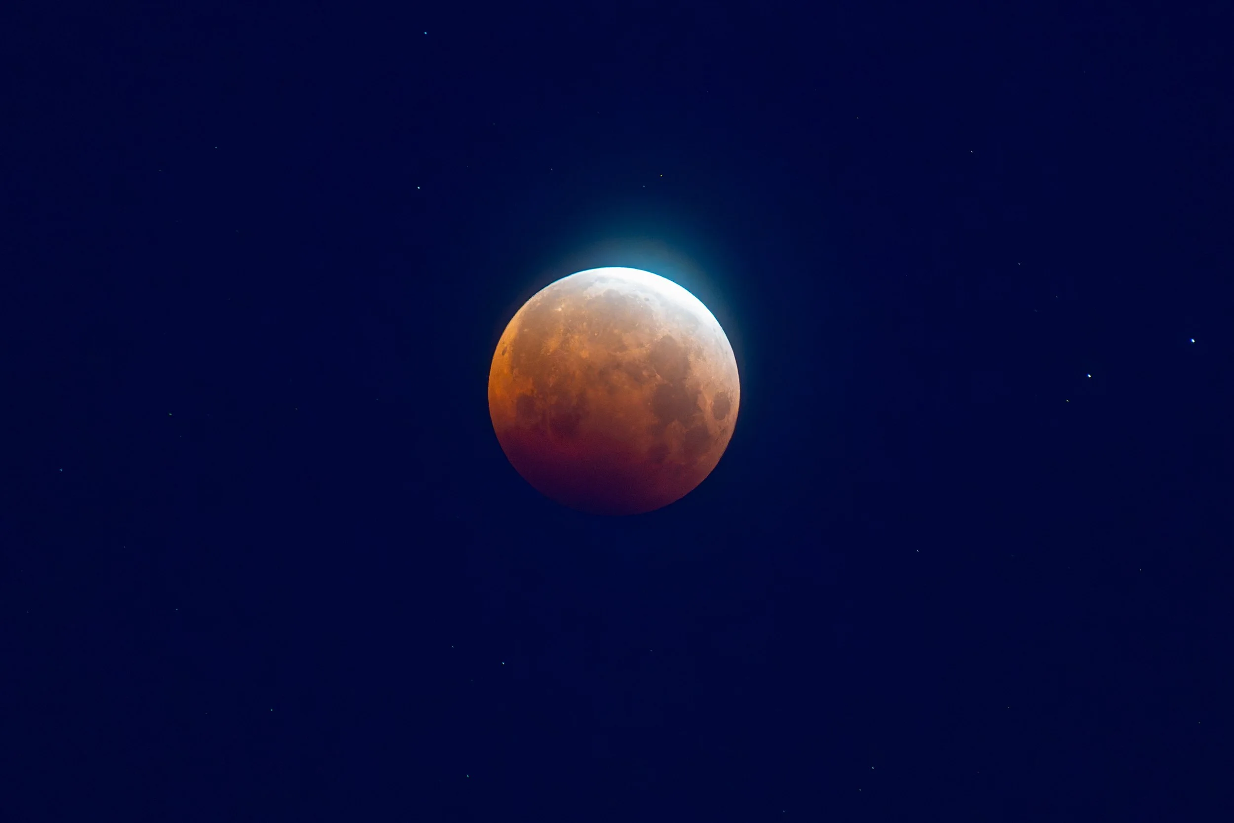 A lunar eclipse showing the moon partially covered with a reddish hue, set against a dark night sky with stars, captured by Andrew Sambuceto Photogaphy