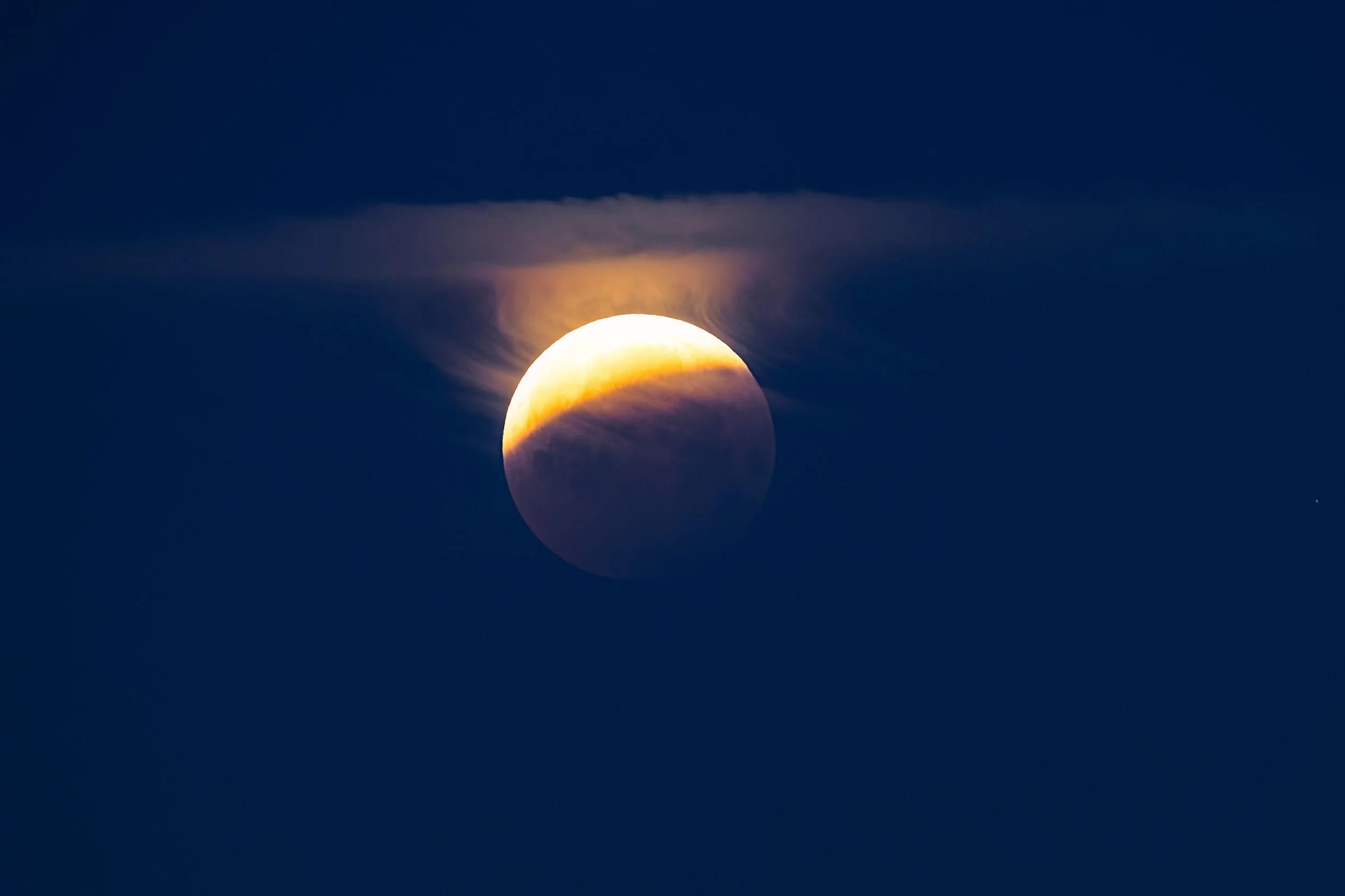 The moon partially obscured by clouds during a lunar eclipse in a dark sky, photographed by Andrew Sambuceto Photography.