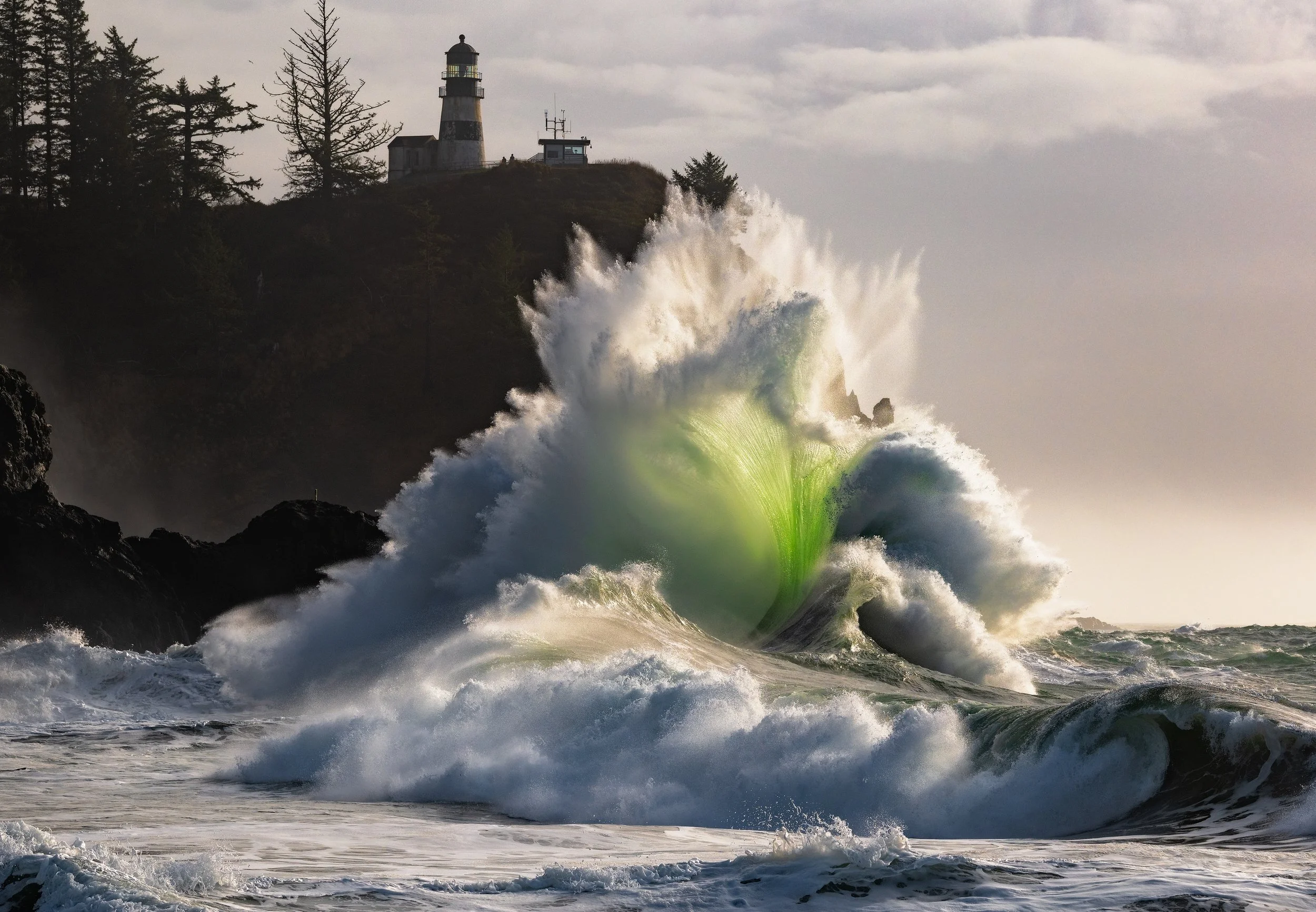 A massive King Tide winter swell exploding on the Pacific Northwest coast, featuring a glowing emerald green backlit wave and a historic lighthouse.