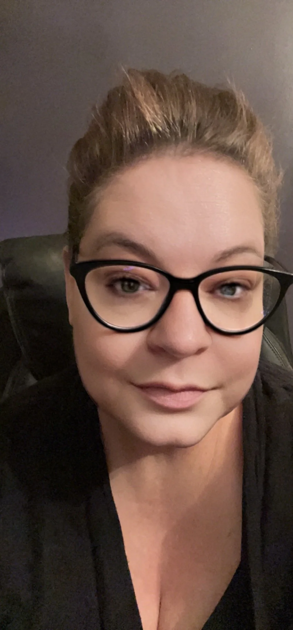A close-up portrait of a woman with blonde hair, blue eyes, light makeup, and a serious expression, wearing a light blue collared shirt.