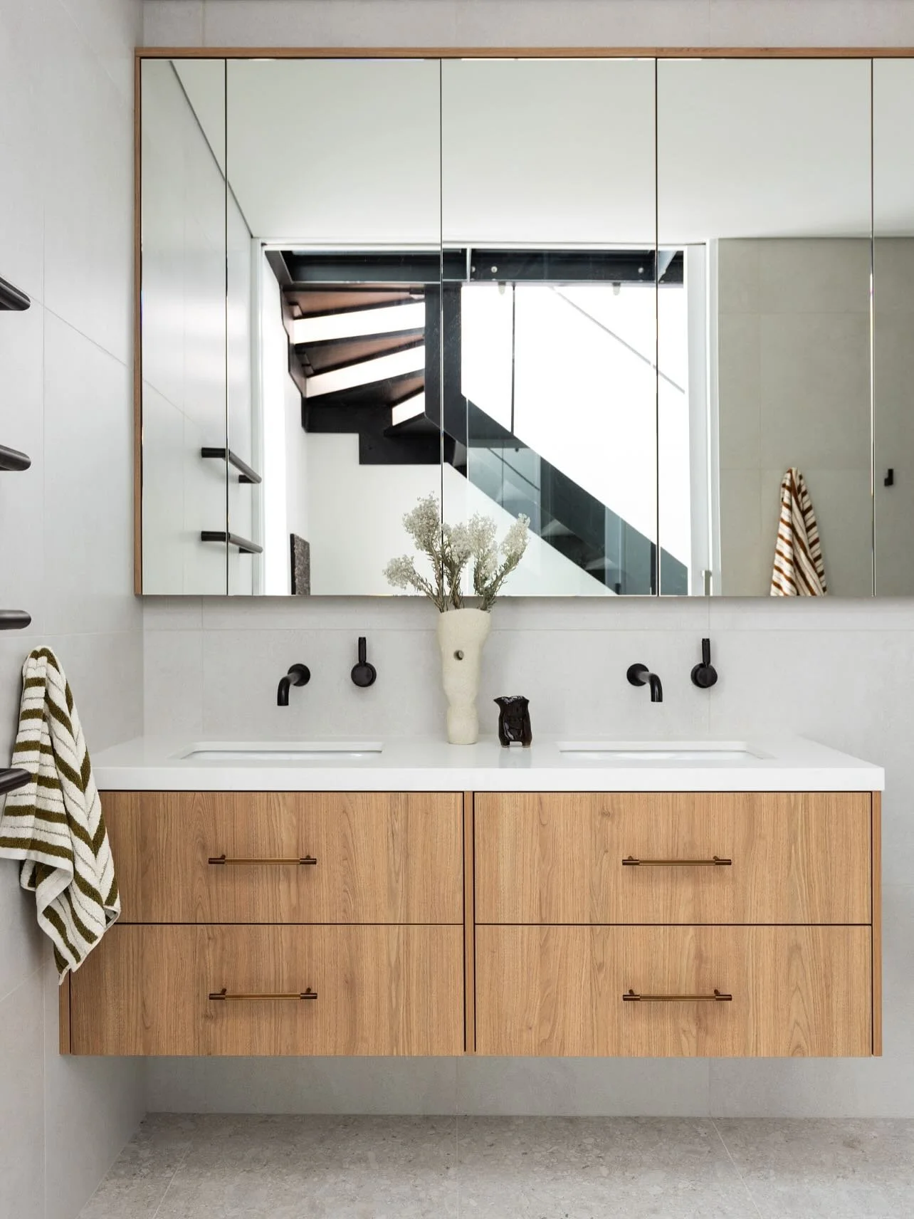Thoughtful design turned a windowless bathroom into a light and airy space.  Large custom mirrored storage and vanity keeps the room calm and clutter free,  while a soft neutral palette gives it a spacious feel.  Layered lighting ensures it stays bri