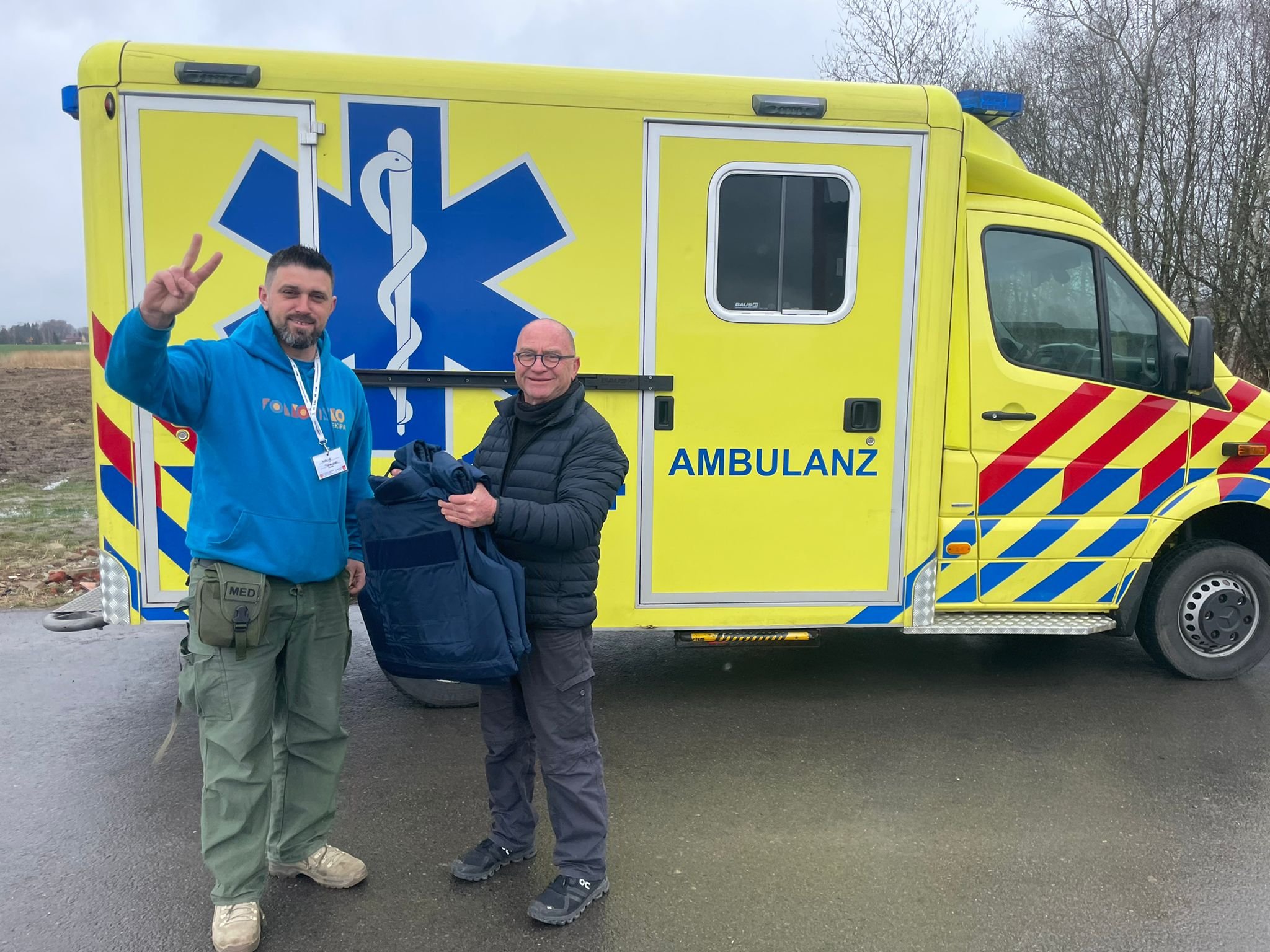 NATAN's Oded Regev presents gift of armored vests to Folkowisko's Marcin Wodzirej Piotrowski in front of one of the ambulances donated by NATAN