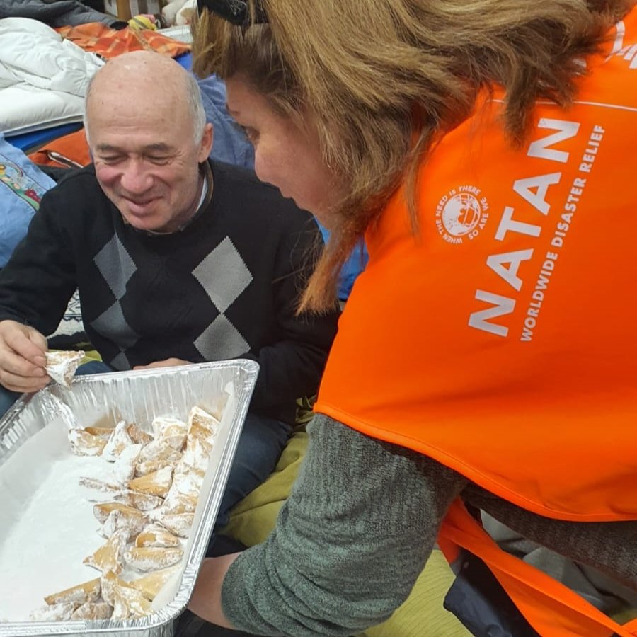 Passing out hamantaschen pastries at the refugee center Purim party