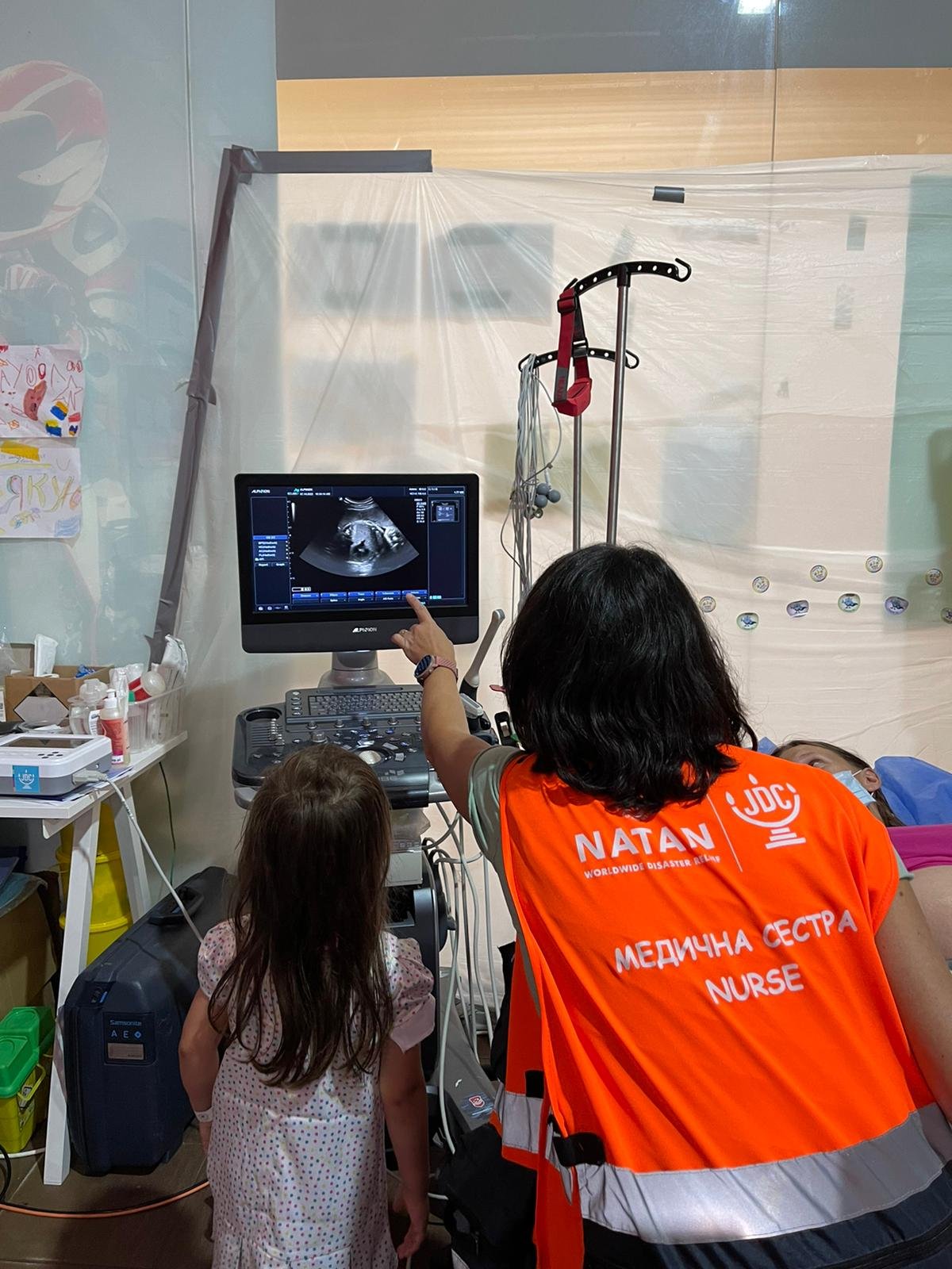 Nurse Midwife Noa Bernat uses portable ultrasound equipment for Point-of-Care Ultrasound (POCUS) to assess the health of a mother and developing baby. Noa shows the mother’s older child her future sibling and lets her hear the heartbeat. A reassuring