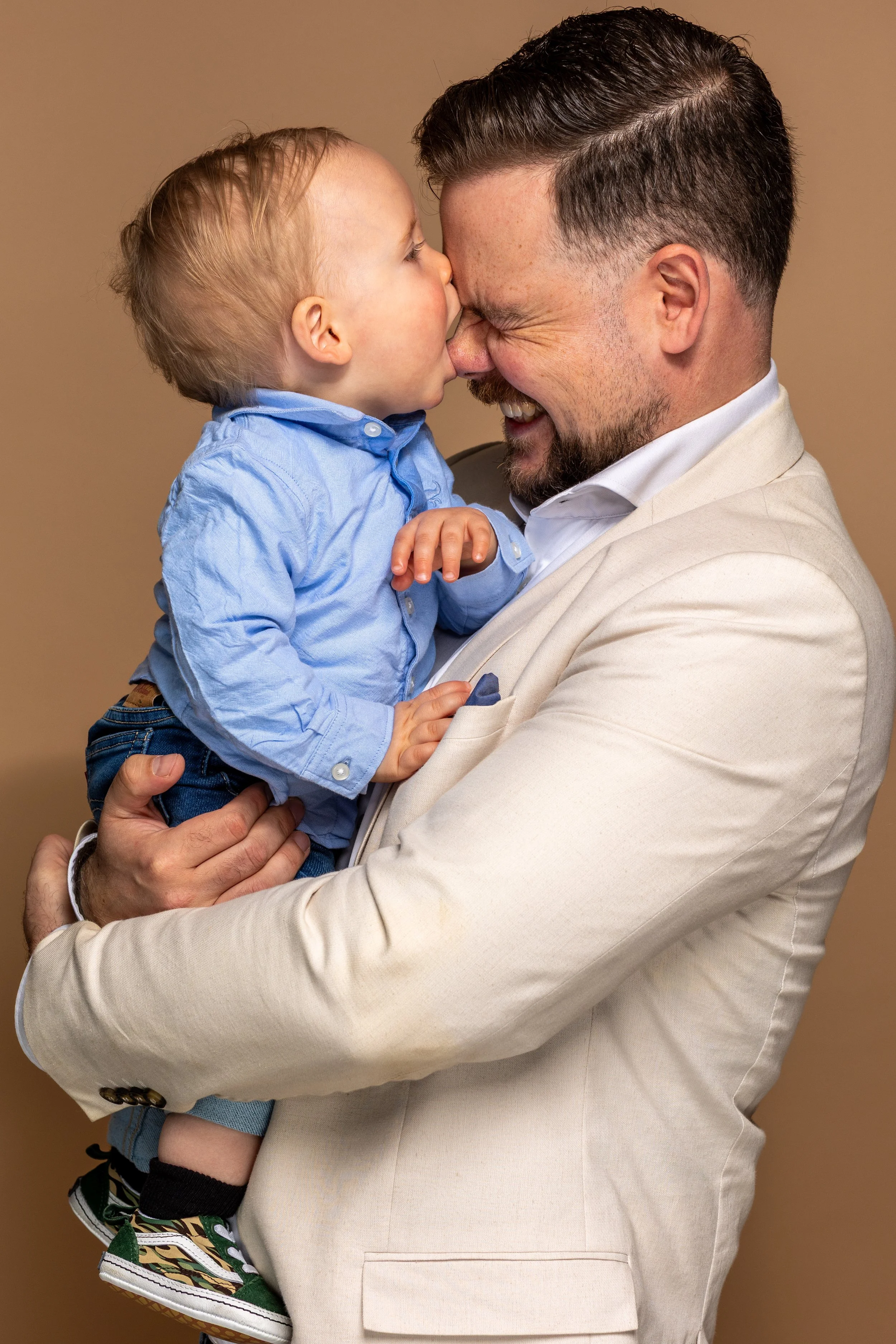 Een man en een kind maken een kus met hun neuzen tegen elkaar, beiden glimlachen.