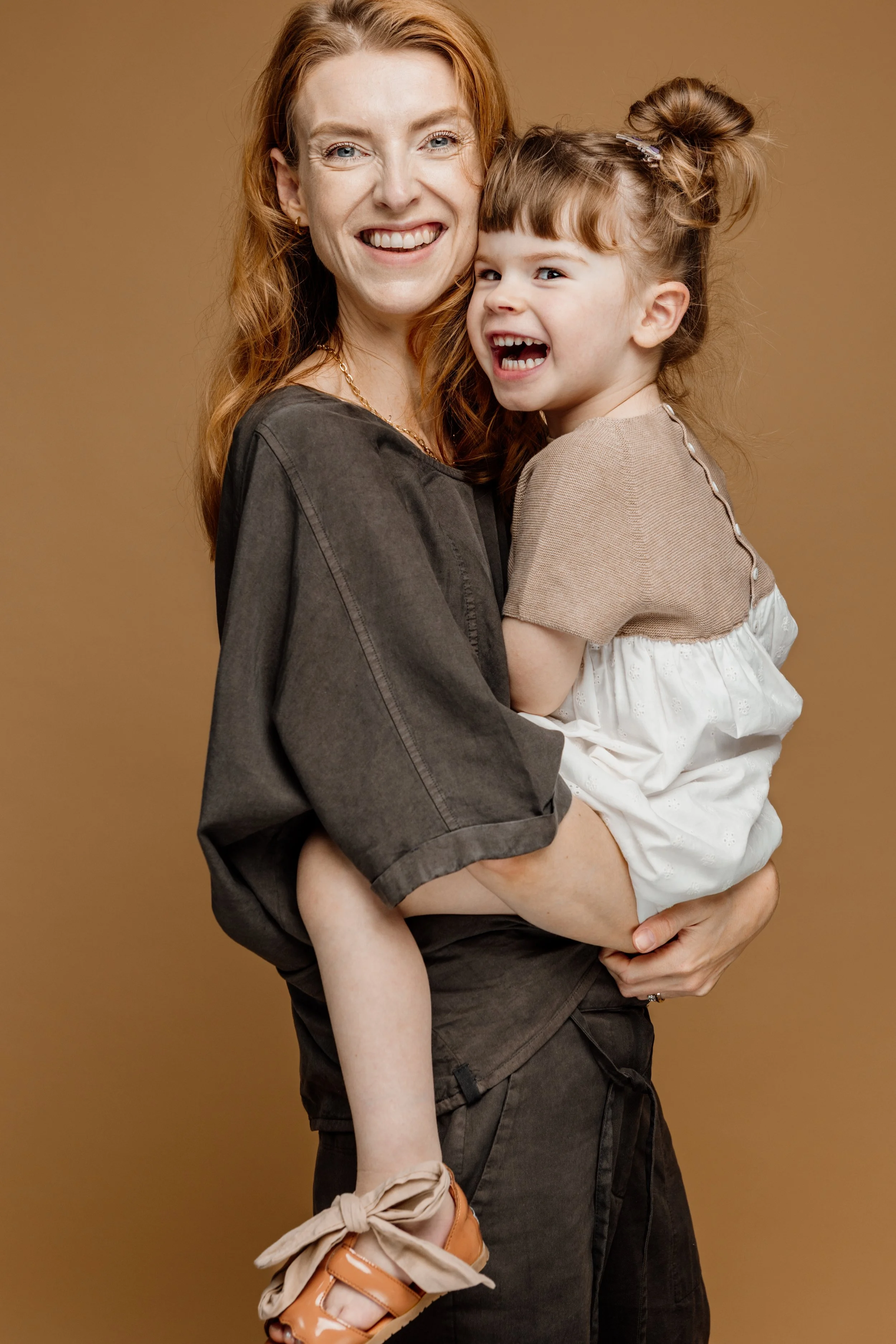 Een vrouw en een jong meisje lachen en knuffelen samen, op een effen beige achtergrond.