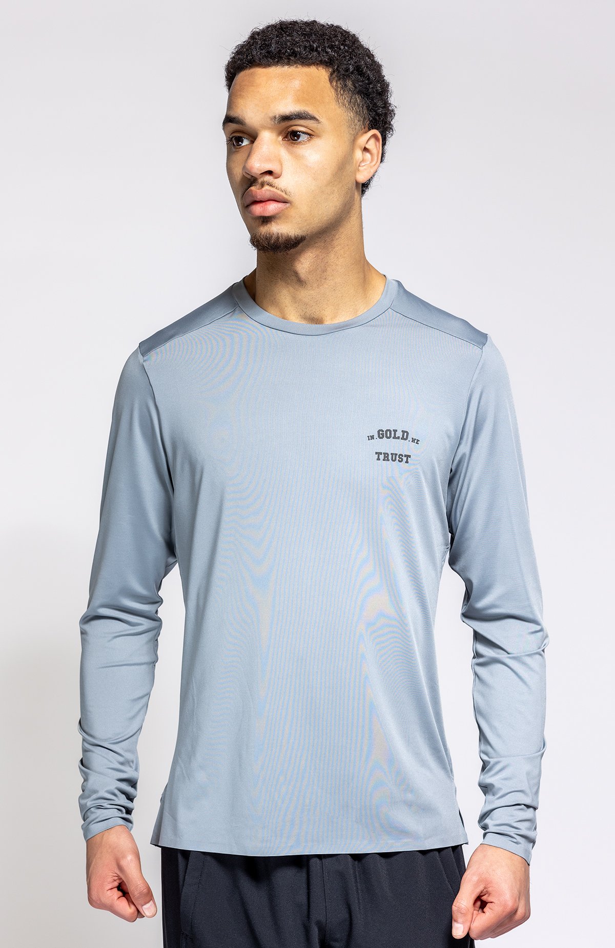 Man in een lichtblauwe sportshirt staat voor een witte achtergrond.