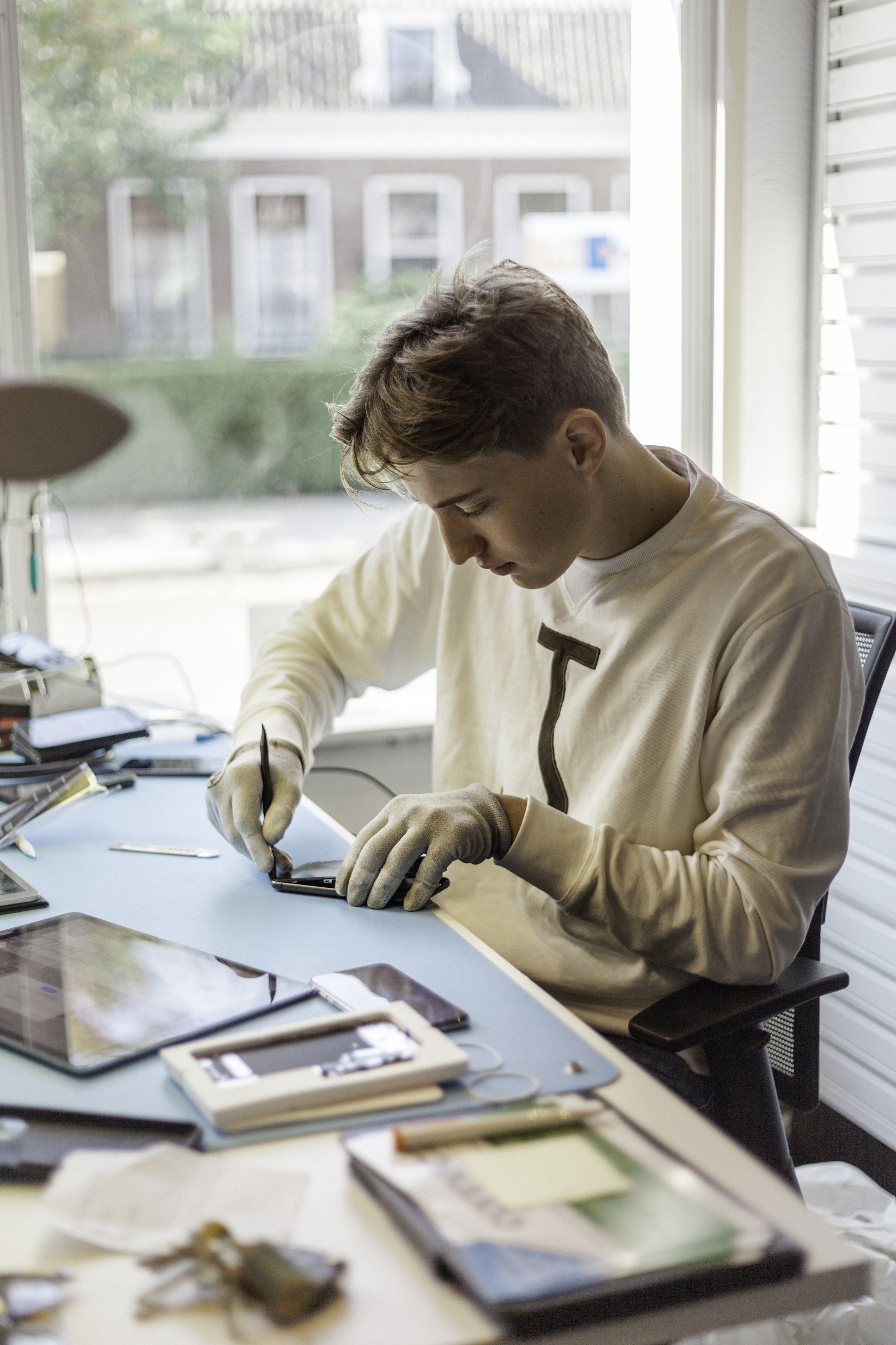 Tienerjongere repareert een smartphone met een gereedschap in een lichte kamer.