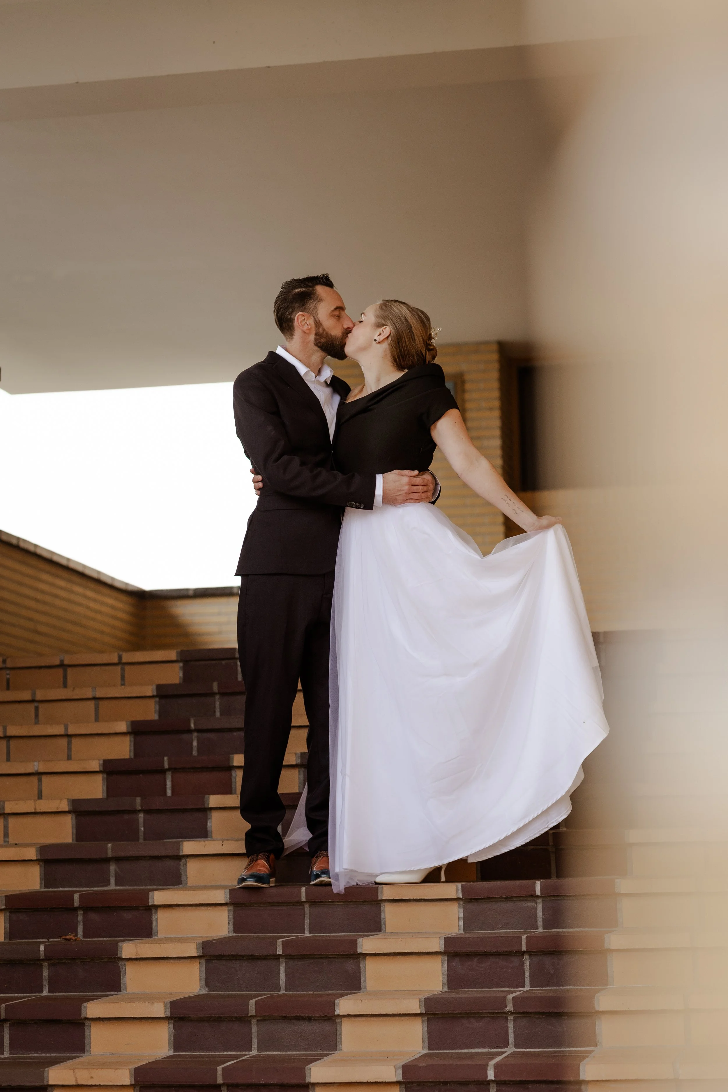 Een bruid en bruidegom kussen elkaar op de trappen van een gebouw op hun trouwdag.