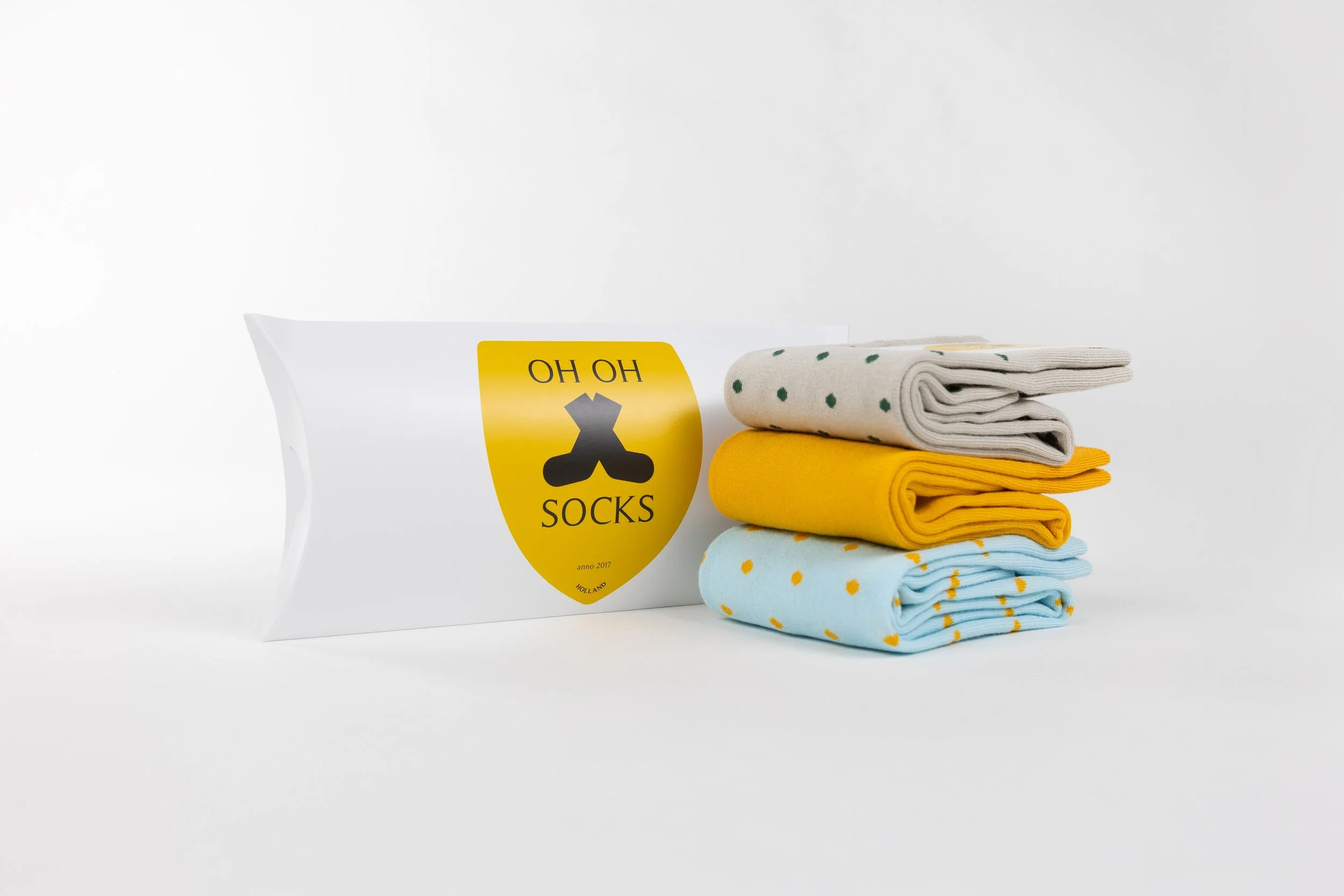 Een set gestapelde kleurrijke sokken naast een witte verpakking met gele en zwarte design, op een witte achtergrond.