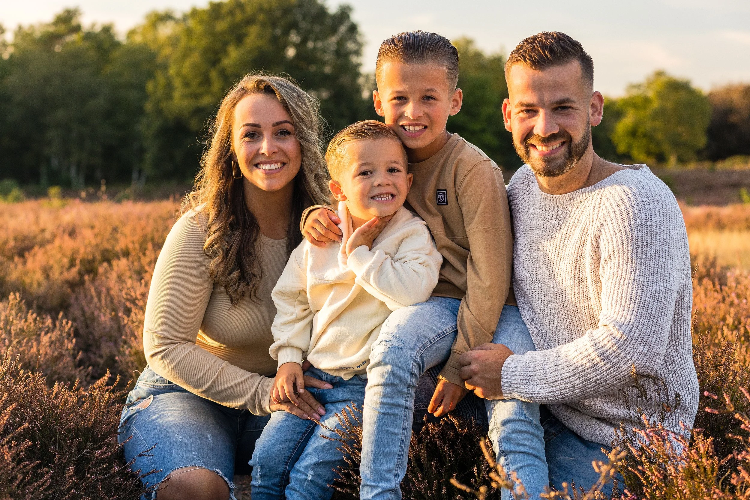 Gezin met twee volwassen mannen en twee jongens op een veld met bloemen, zonsondergang