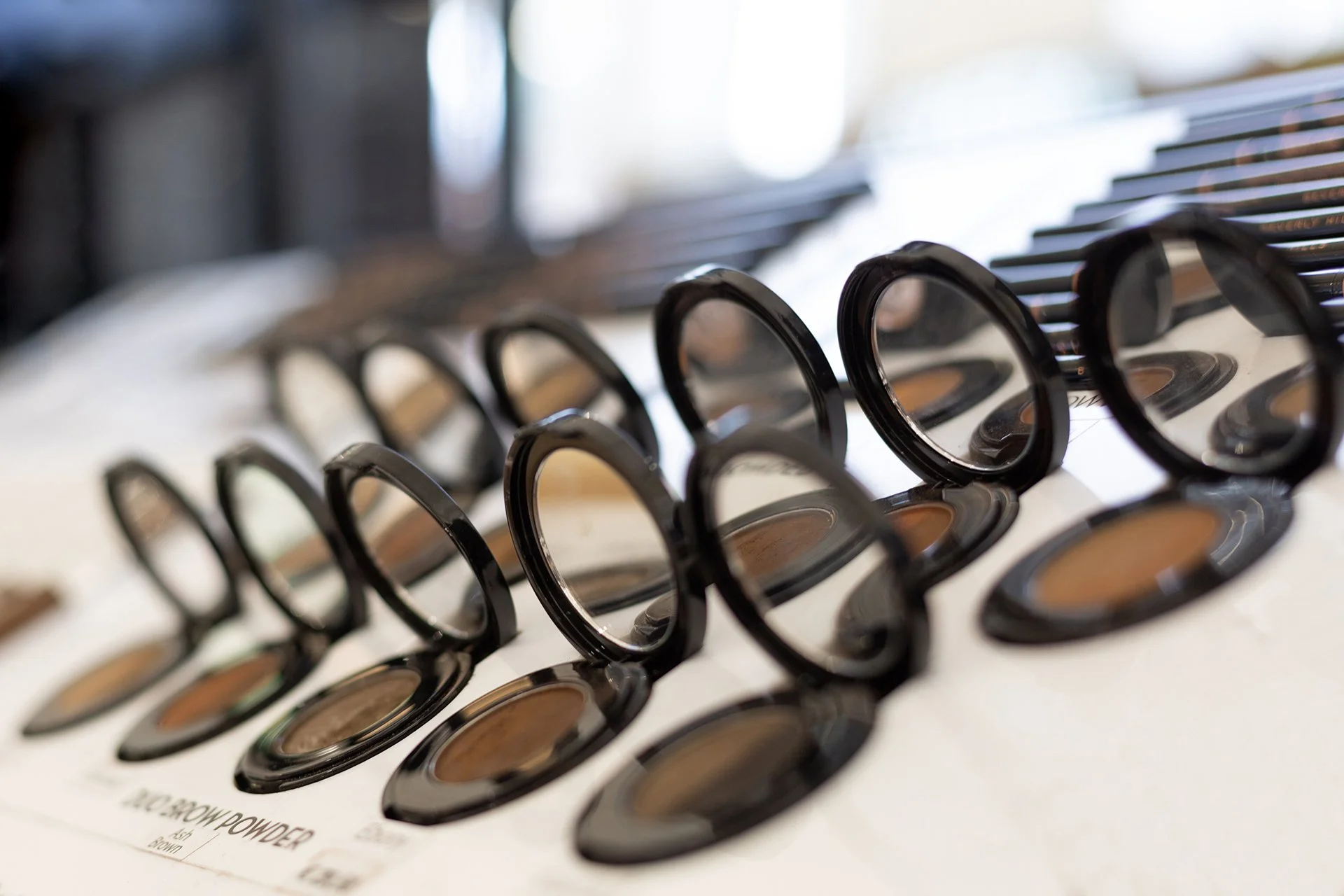 Verzameling make-up oogschaduw potjes met ronde zwarte deksels op een witte displayplaat.