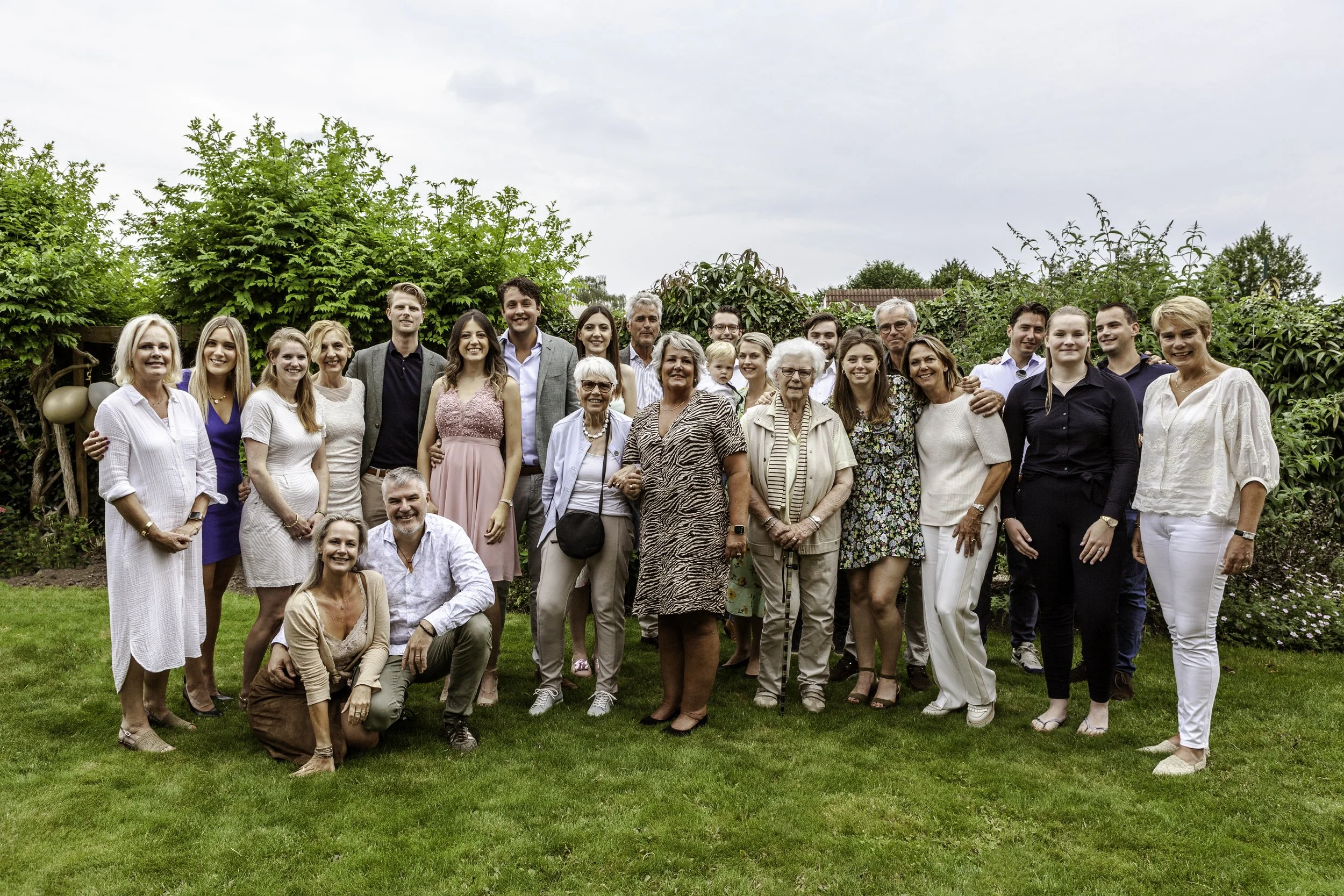 Gezinnen en vrienden samen op een groene tuin, lachend en poseren voor een groepsfoto.