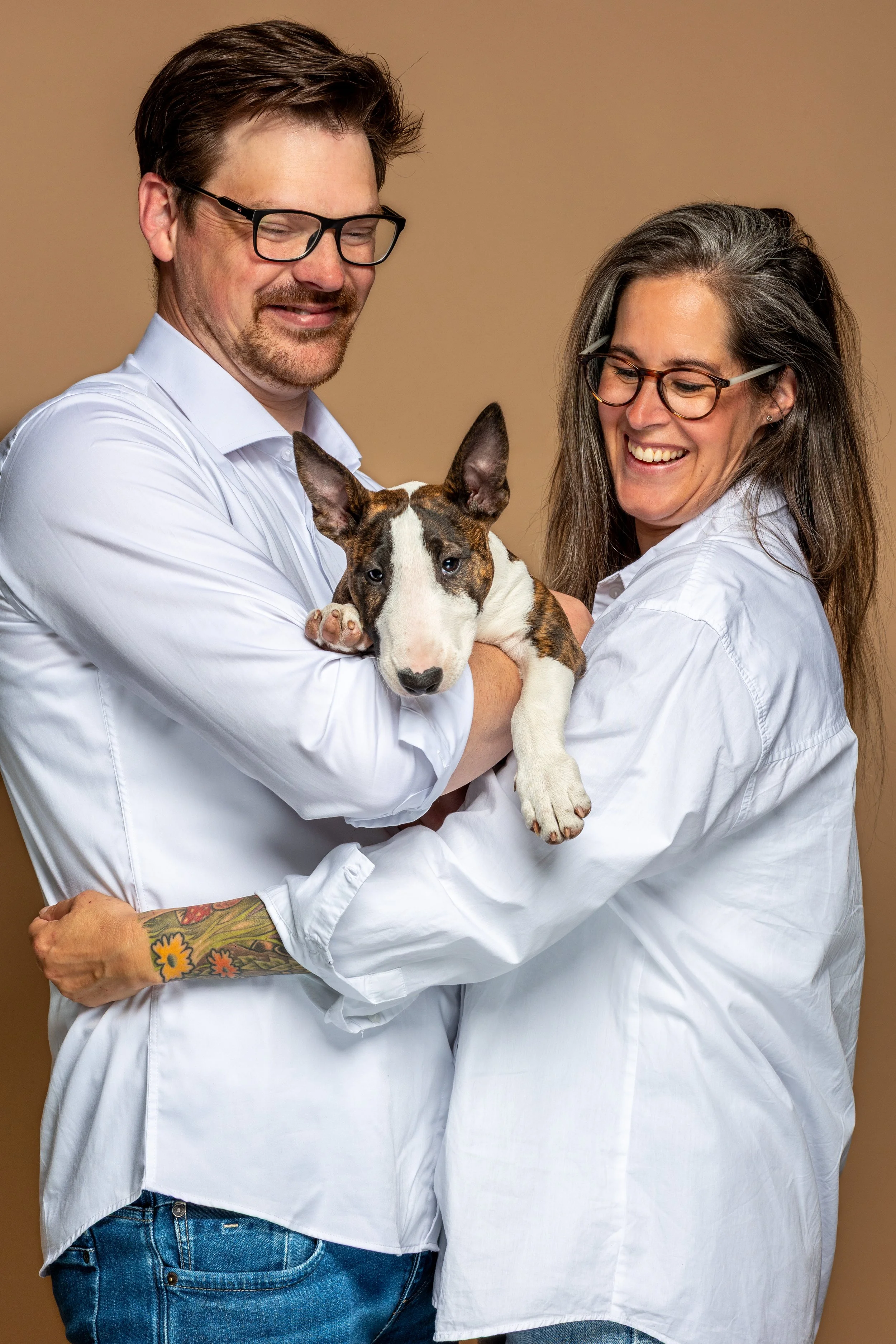 Twee mensen, een man en een vrouw, houden samen een jonge puppy van een bontkleurige vacht en grote oren.