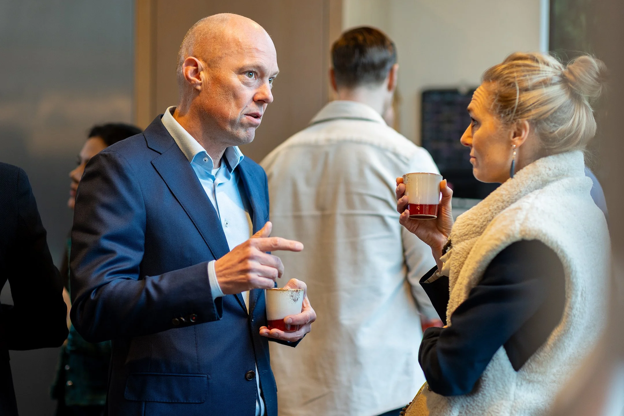 Twee mensen die in een gesprek verwikkeld zijn tijdens een netwerkbijeenkomst, zwaaiend met bekers met warme dranken.
