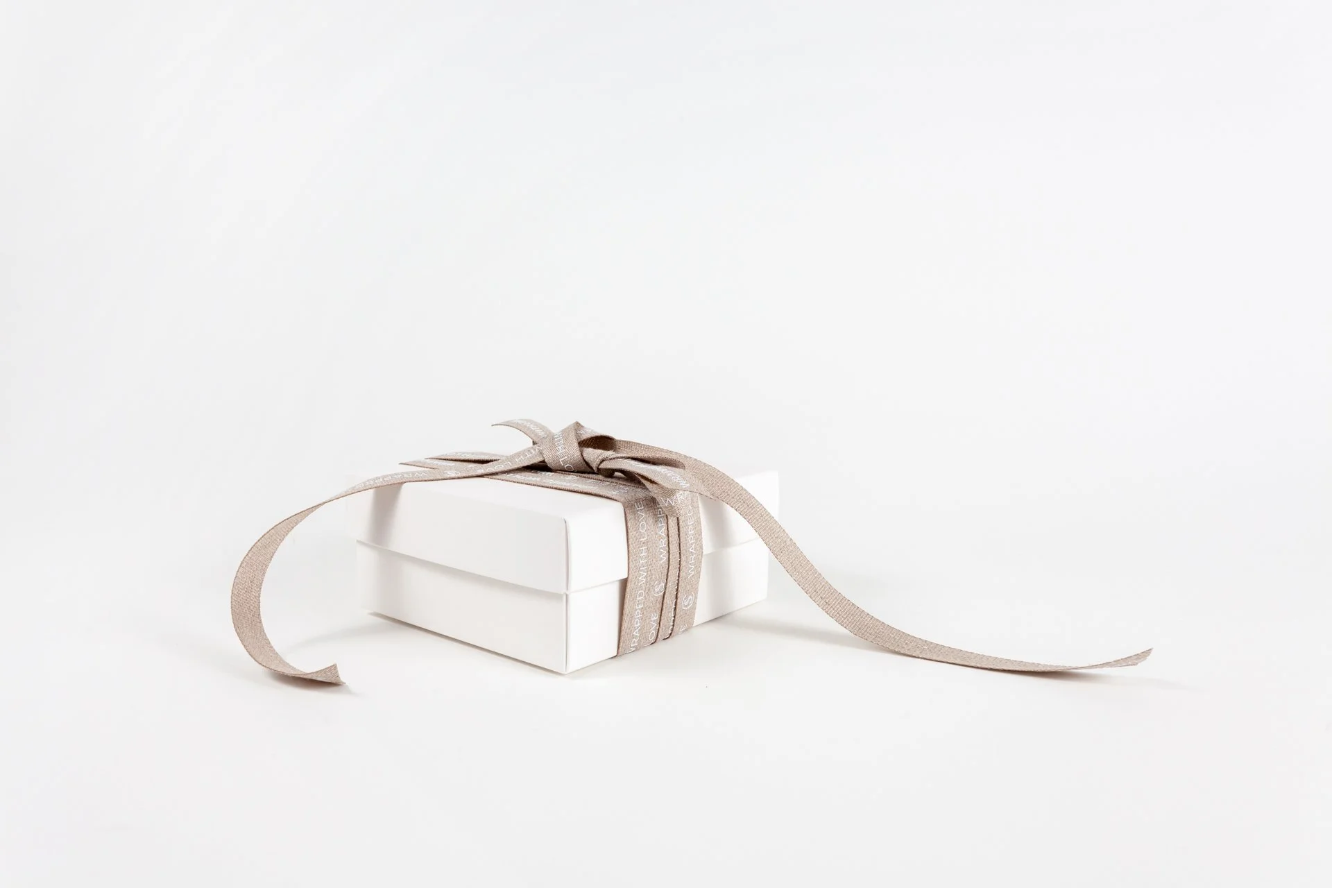 Wit cadeaudoos met beige lint op een witte achtergrond.