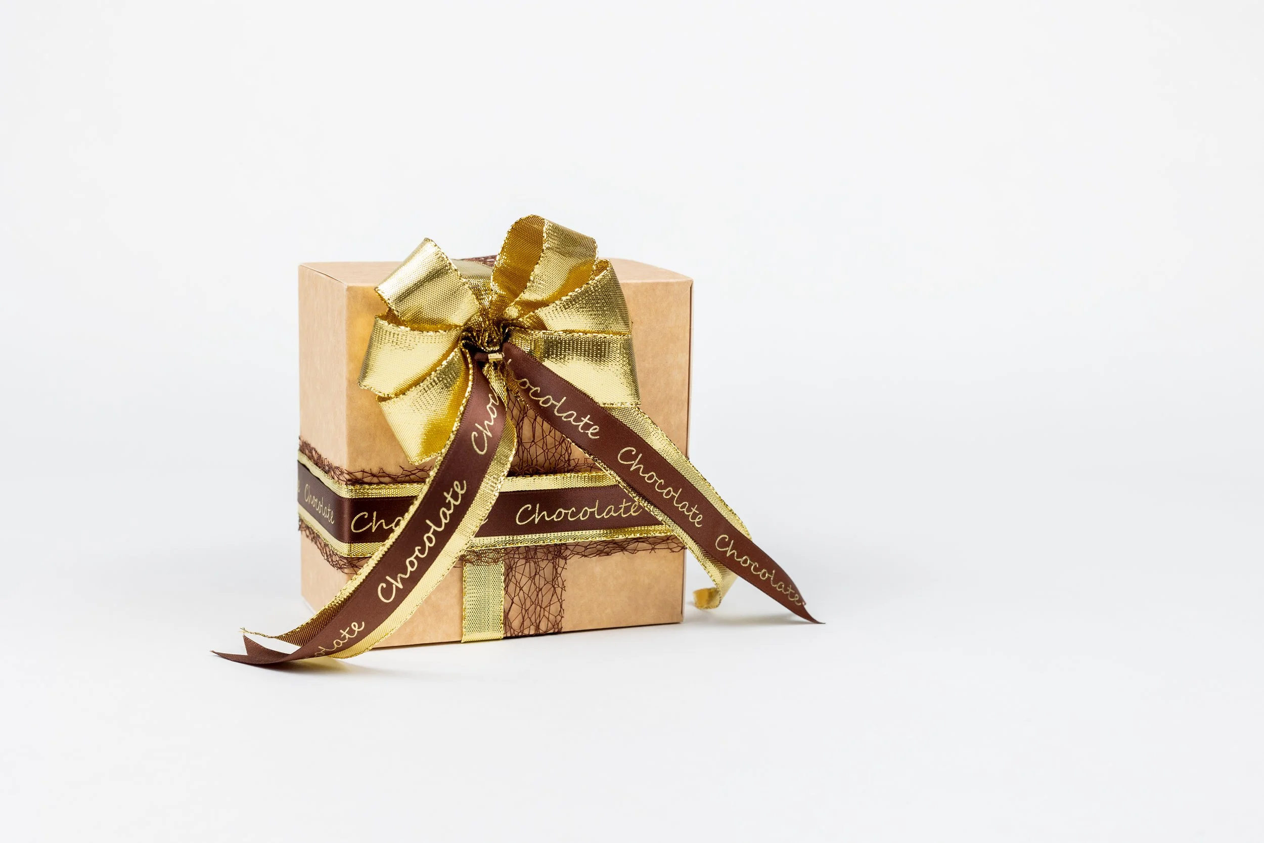 Een geschenkdoos met een goudkleurige lint en een donkerbruin lint met de tekst 'Chocolate' erop, geplaatst op een witte achtergrond.