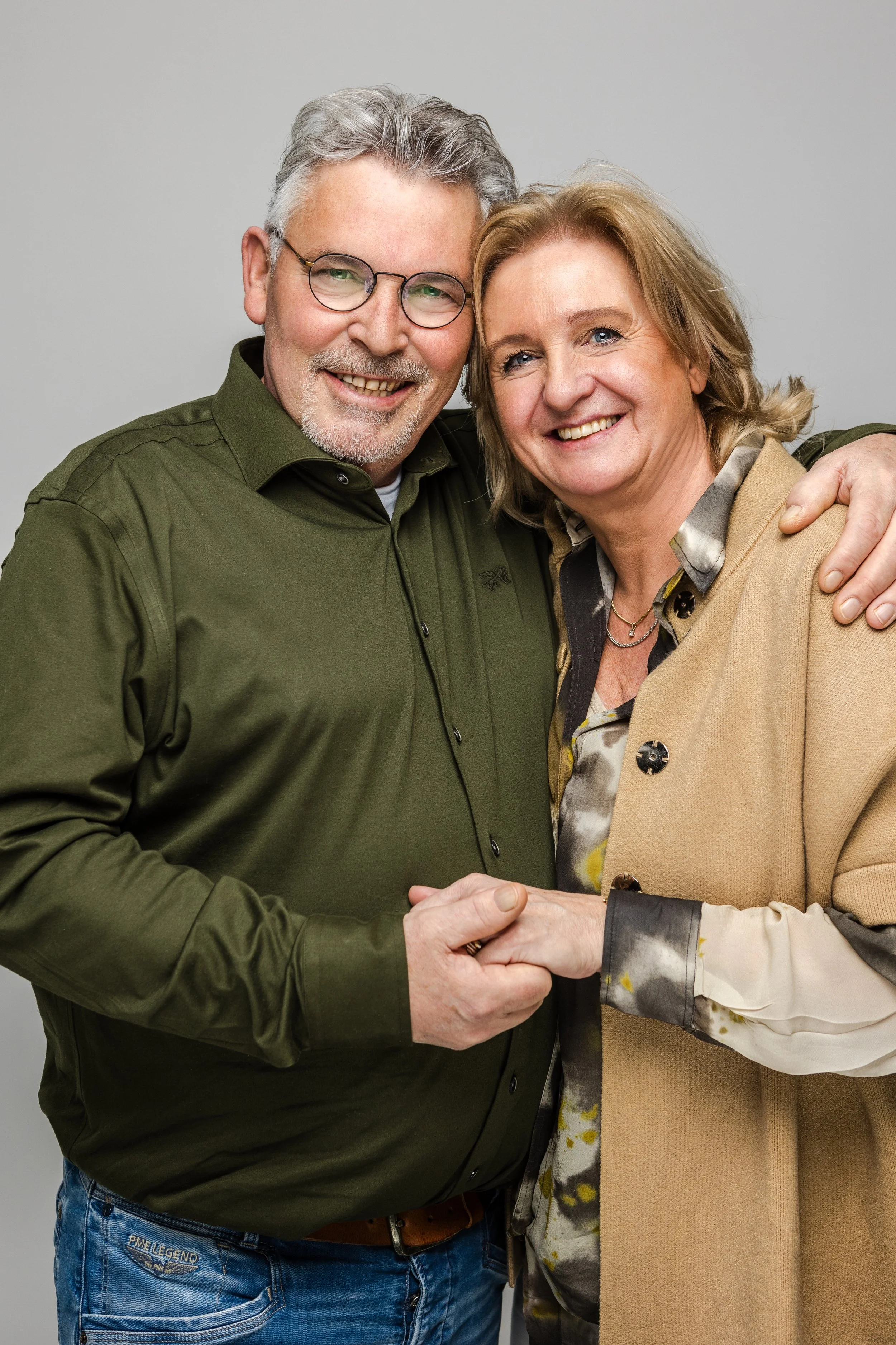 Een man en een vrouw die elkaar vasthouden en glimlachen, tegen een neutrale achtergrond.