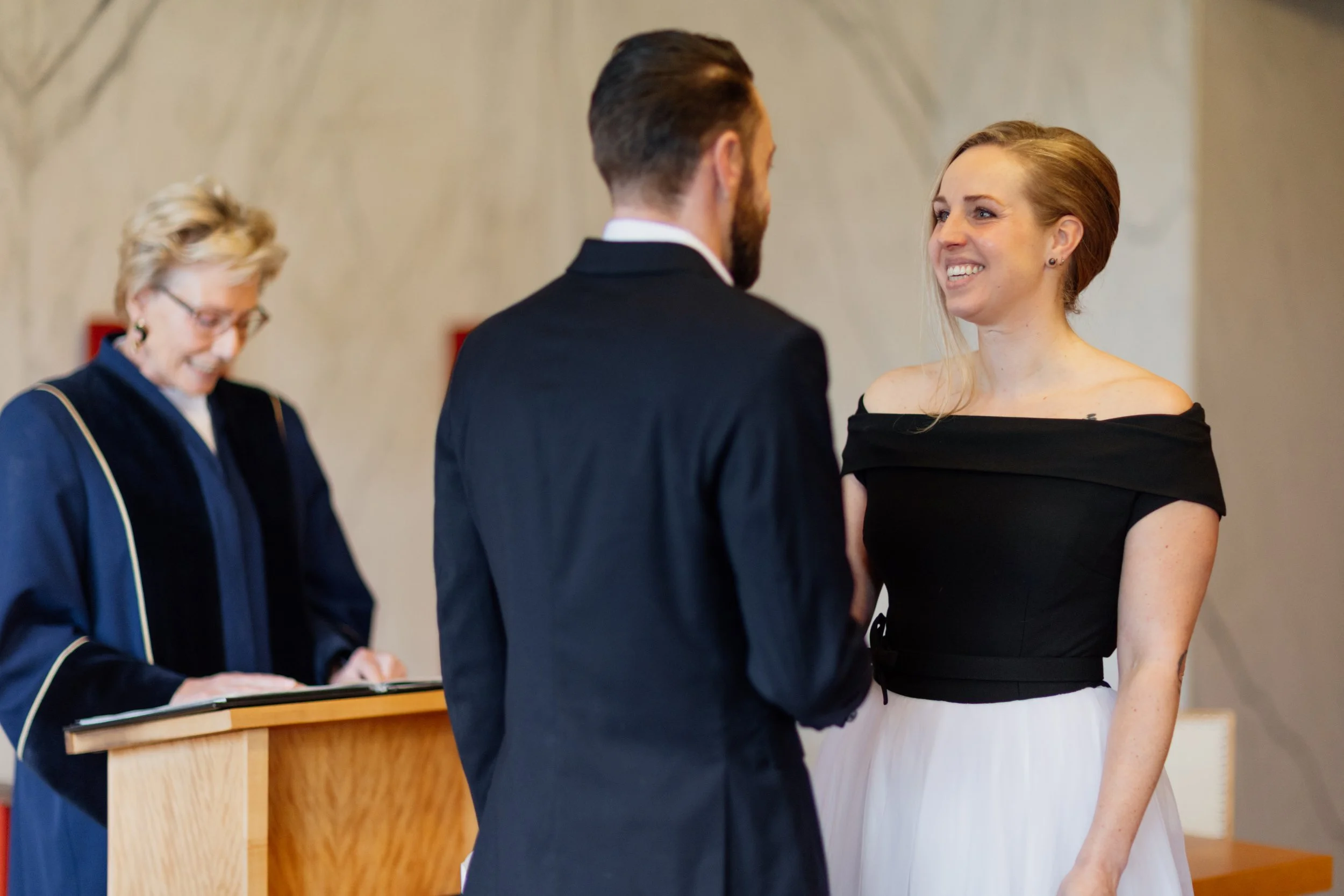 Een bruid en bruidegom tijdens hun huwelijksceremonie met een officiant op de achtergrond.