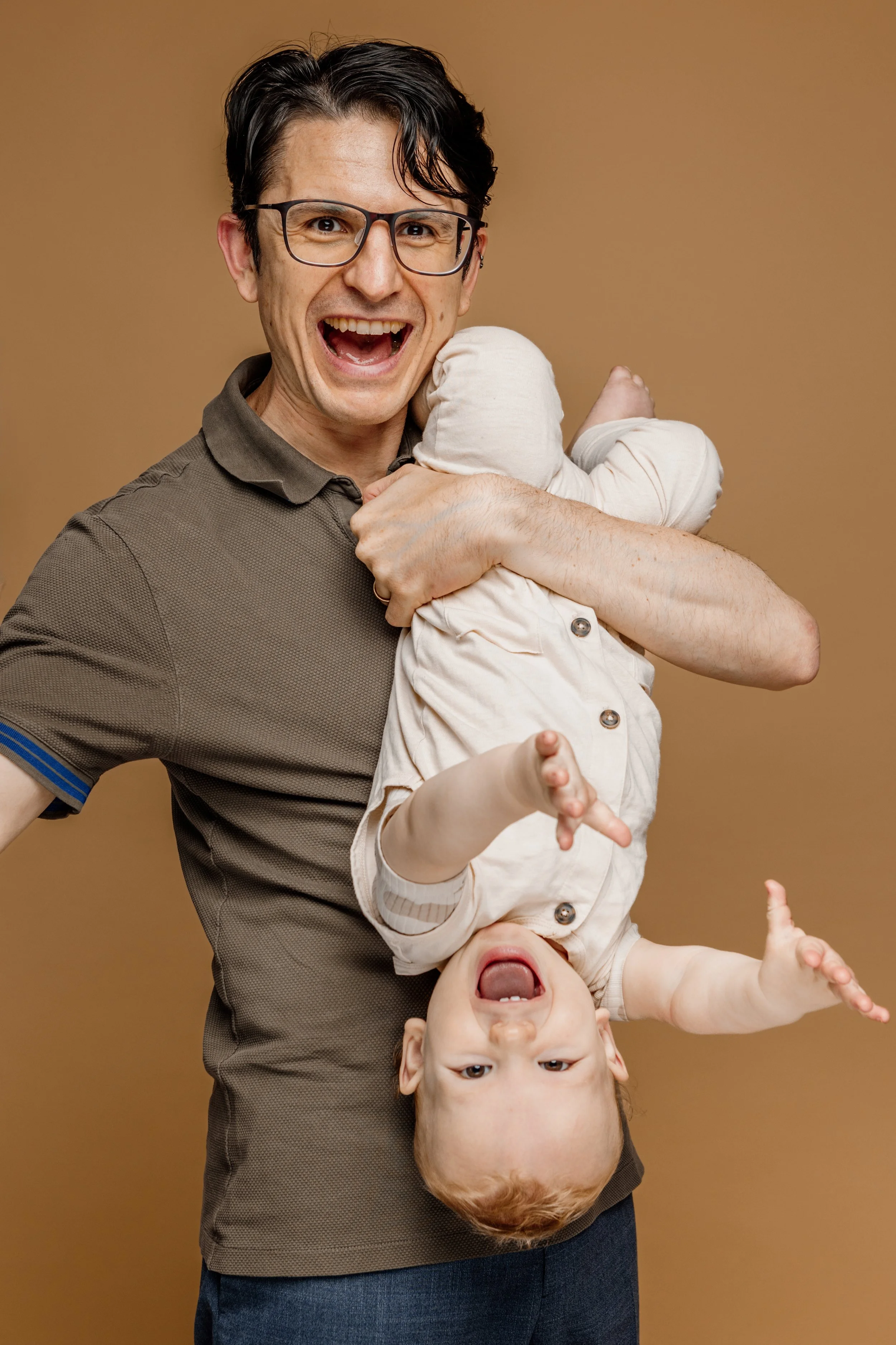 Man met bril die een kind vasthoudt, het kind hangt ondersteboven en lacht.