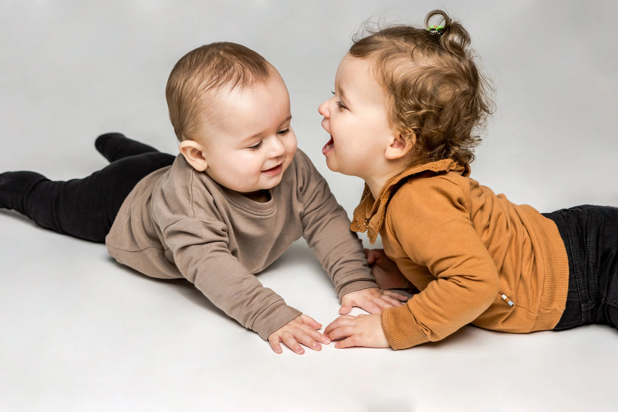 Twee jonge kinderen liggen op de grond, elkaar lachend en schreeuwend, in een speelse interactie.