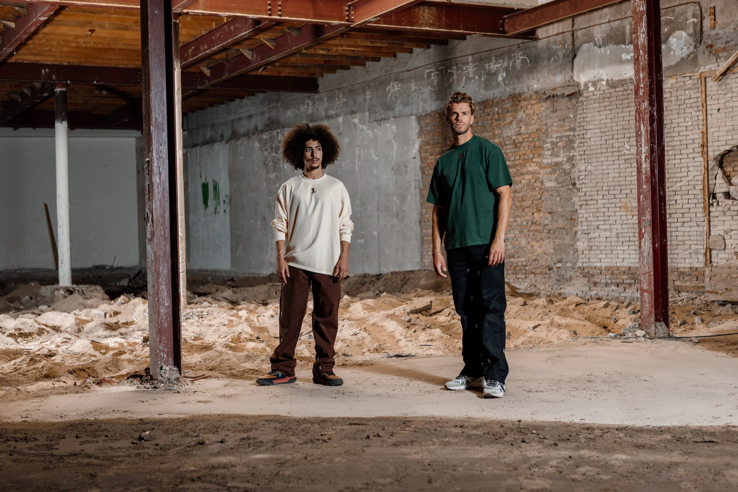 Twee jonge mannen staan in een bouwvallige ruimte met ruwe muren en stoeptegels op de vloer.